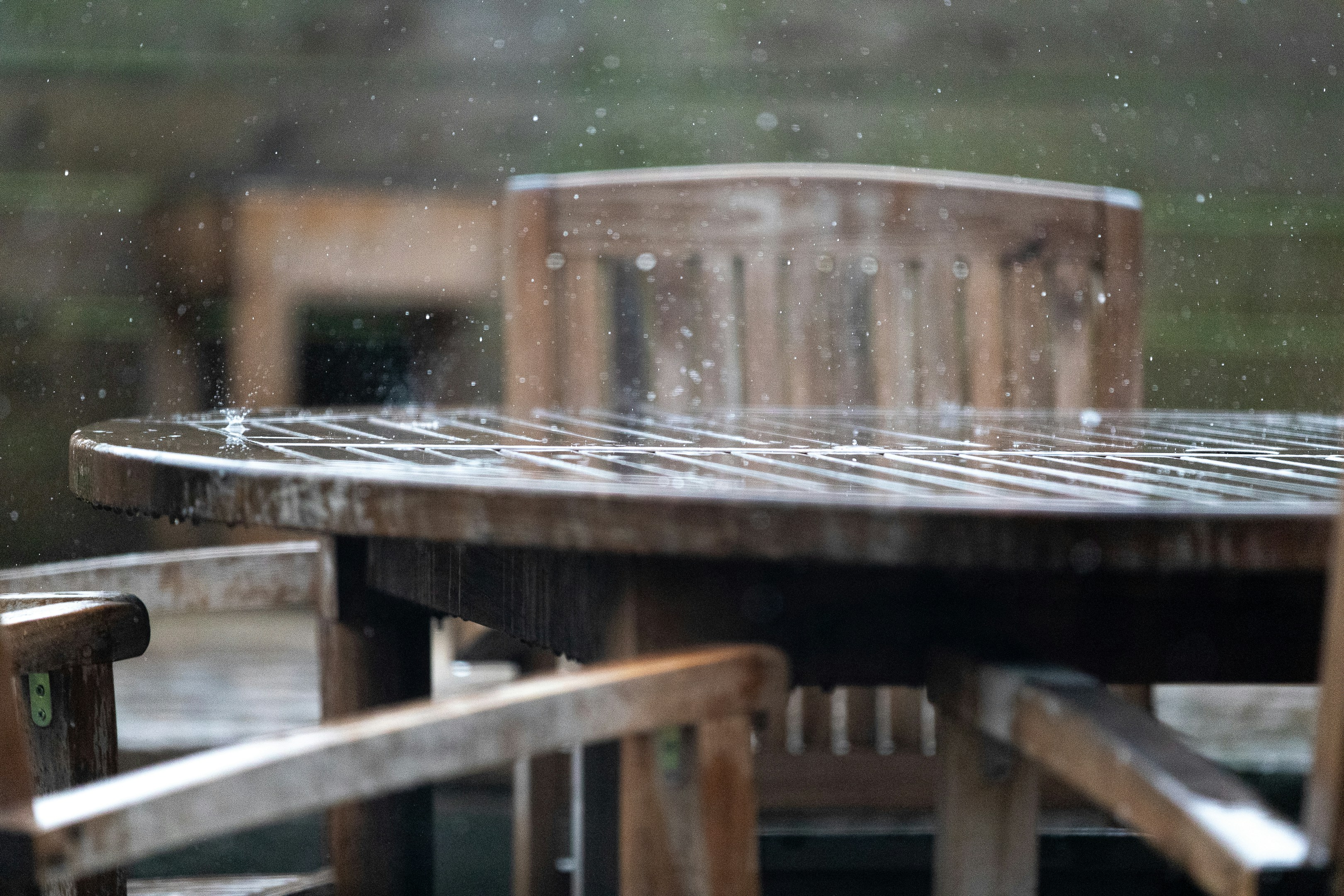 La pluie tombe sur une table extérieure en bois et des chaises