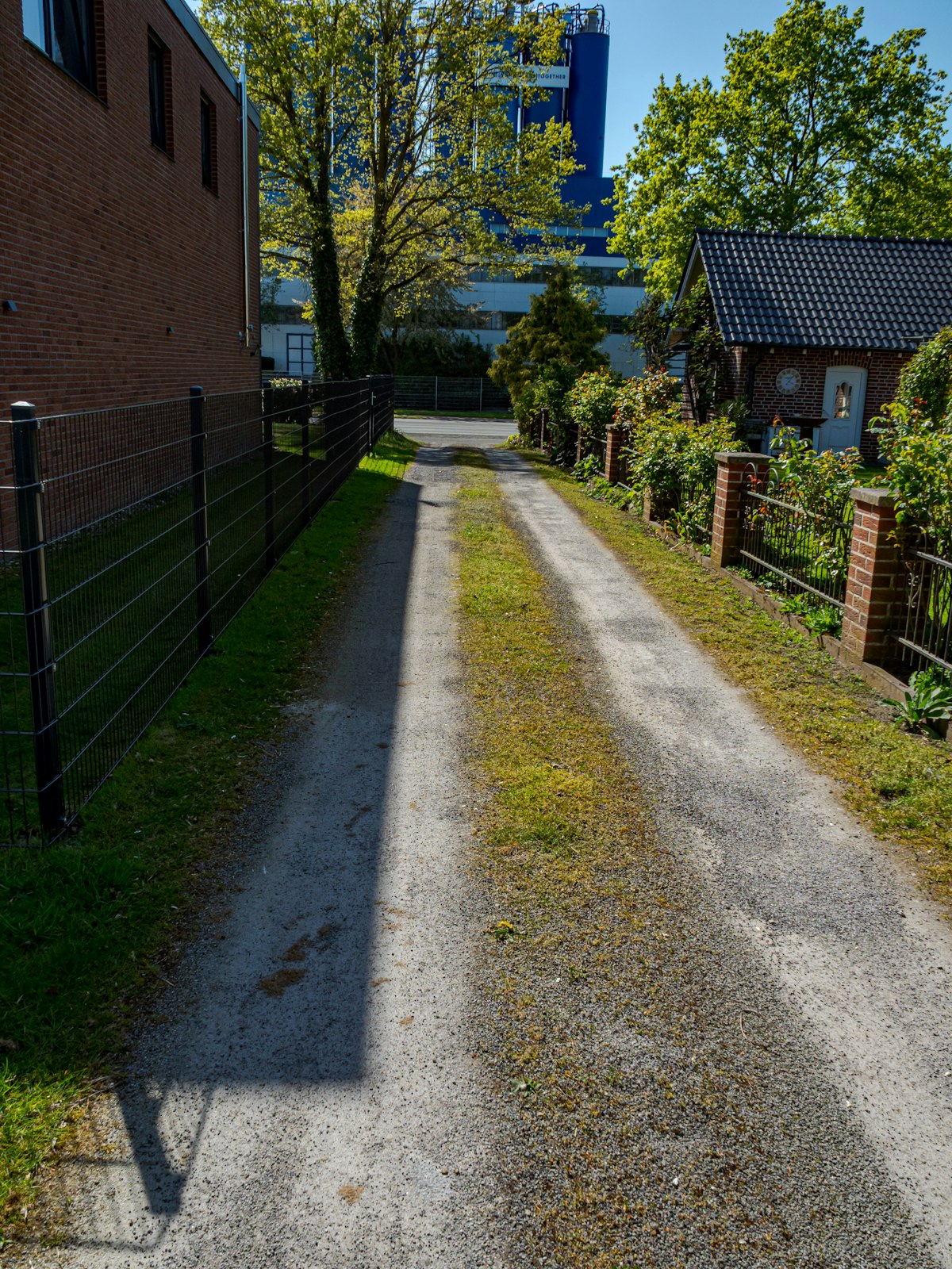 Gravel residential access lane with a grassy center strip beside fences and buildings.