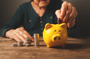 Elderly hands depositing coins into a yellow piggy bank