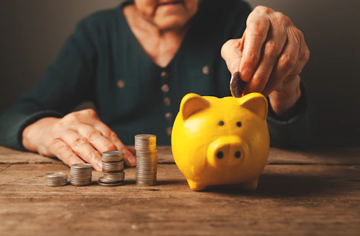 Elderly hands depositing coins into a yellow piggy bank