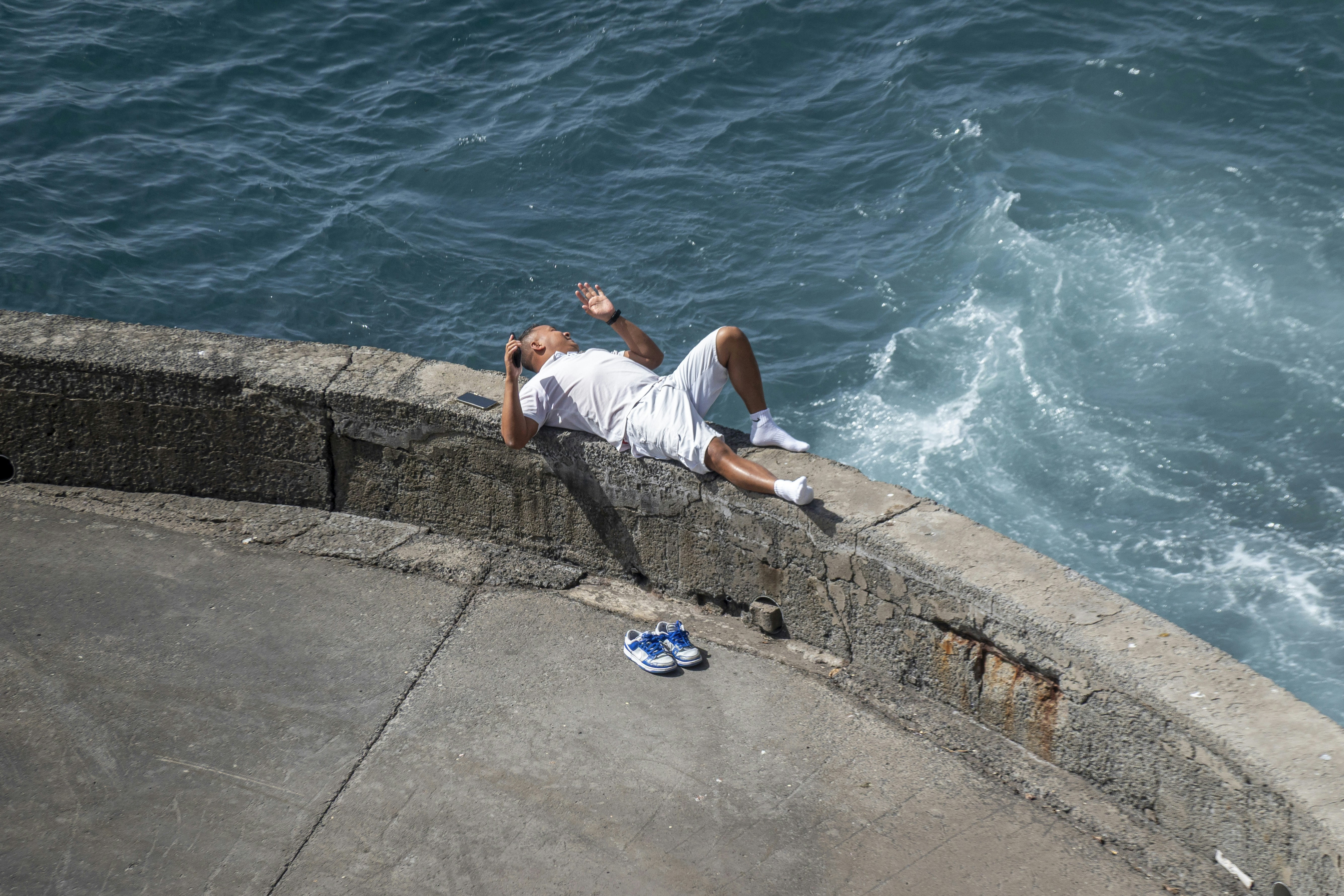 Man in white shorts rests by the blue ocean.