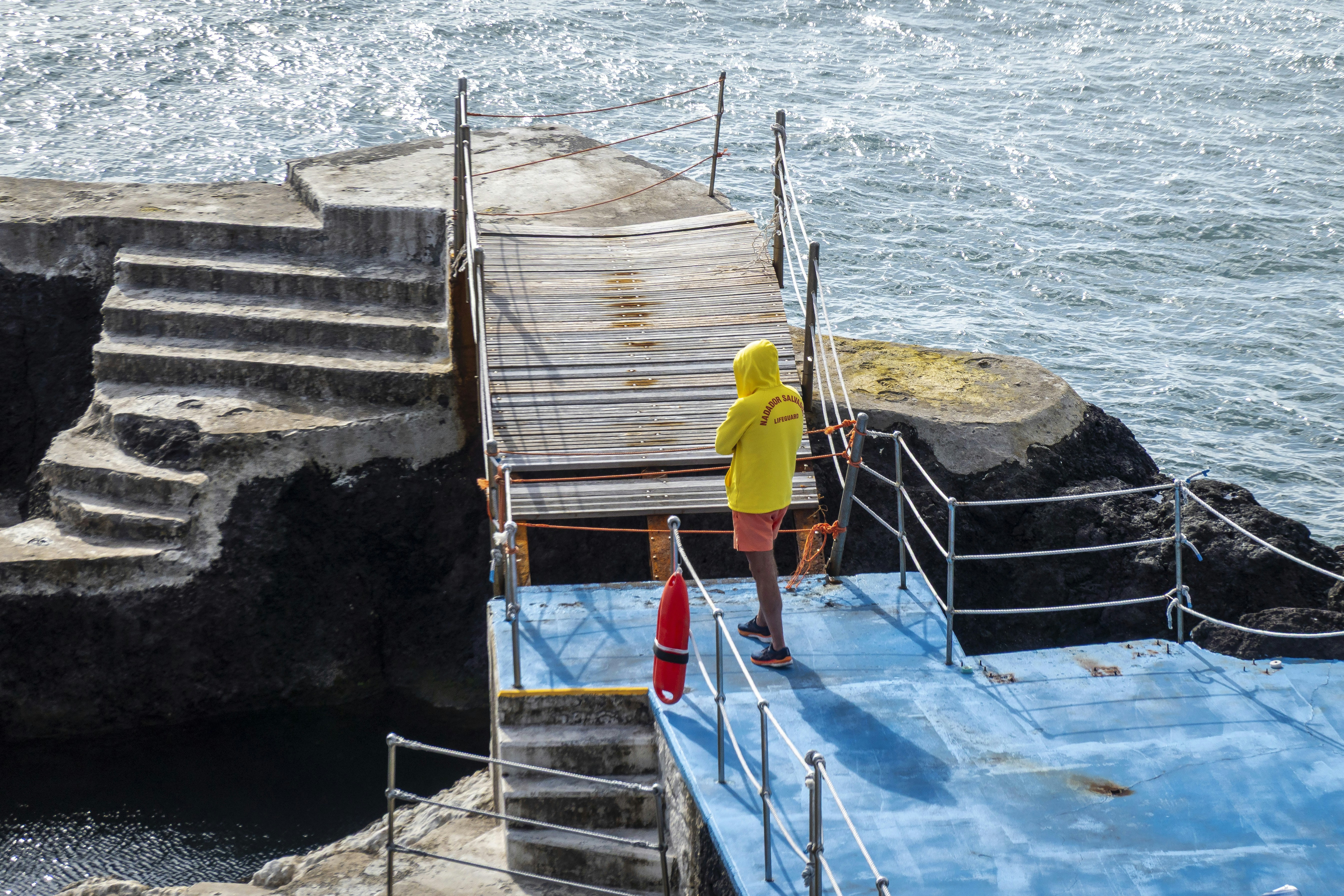 Person in yellow hoodie stands on blue diving board.