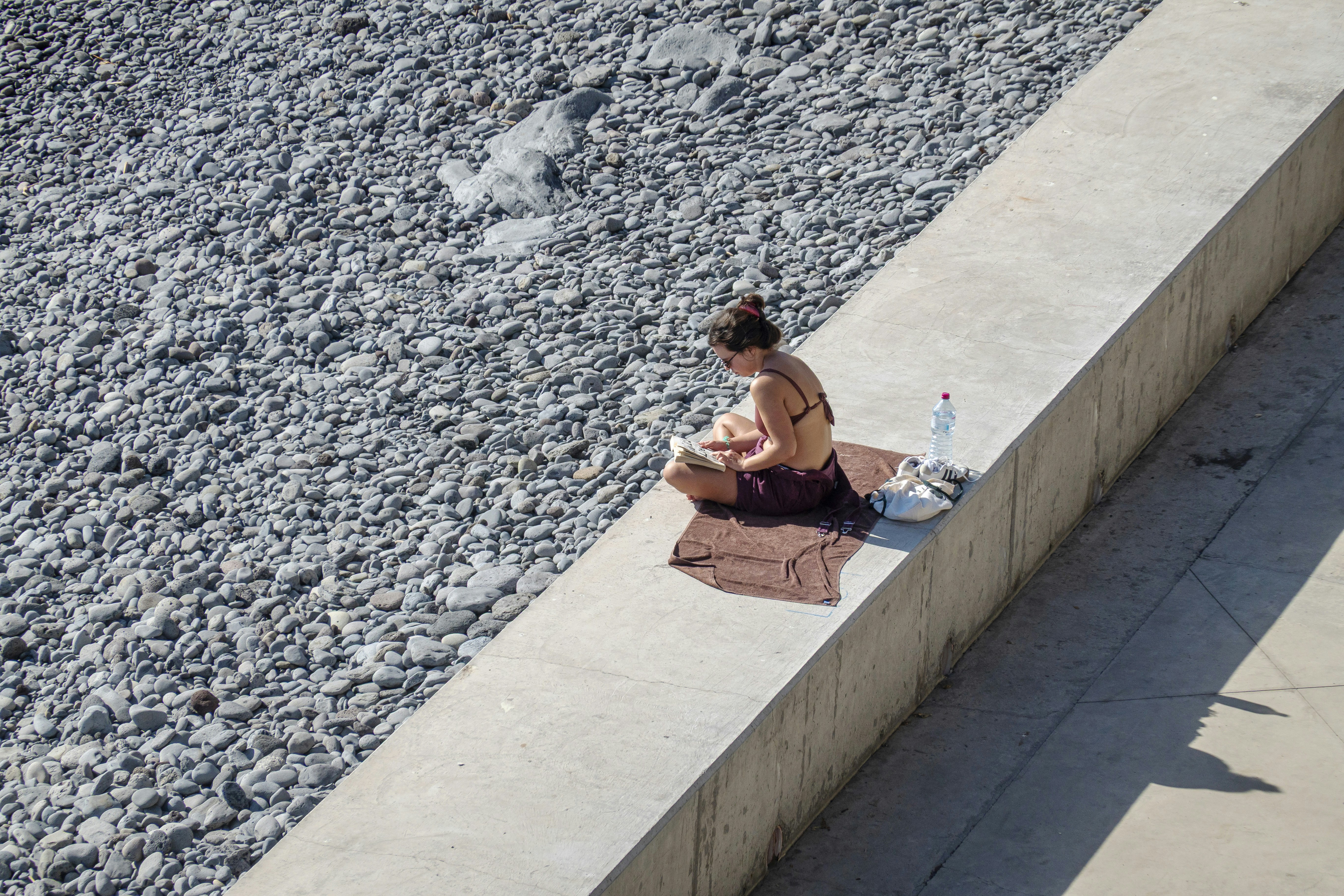 Woman reading on a sunlit ledge near water