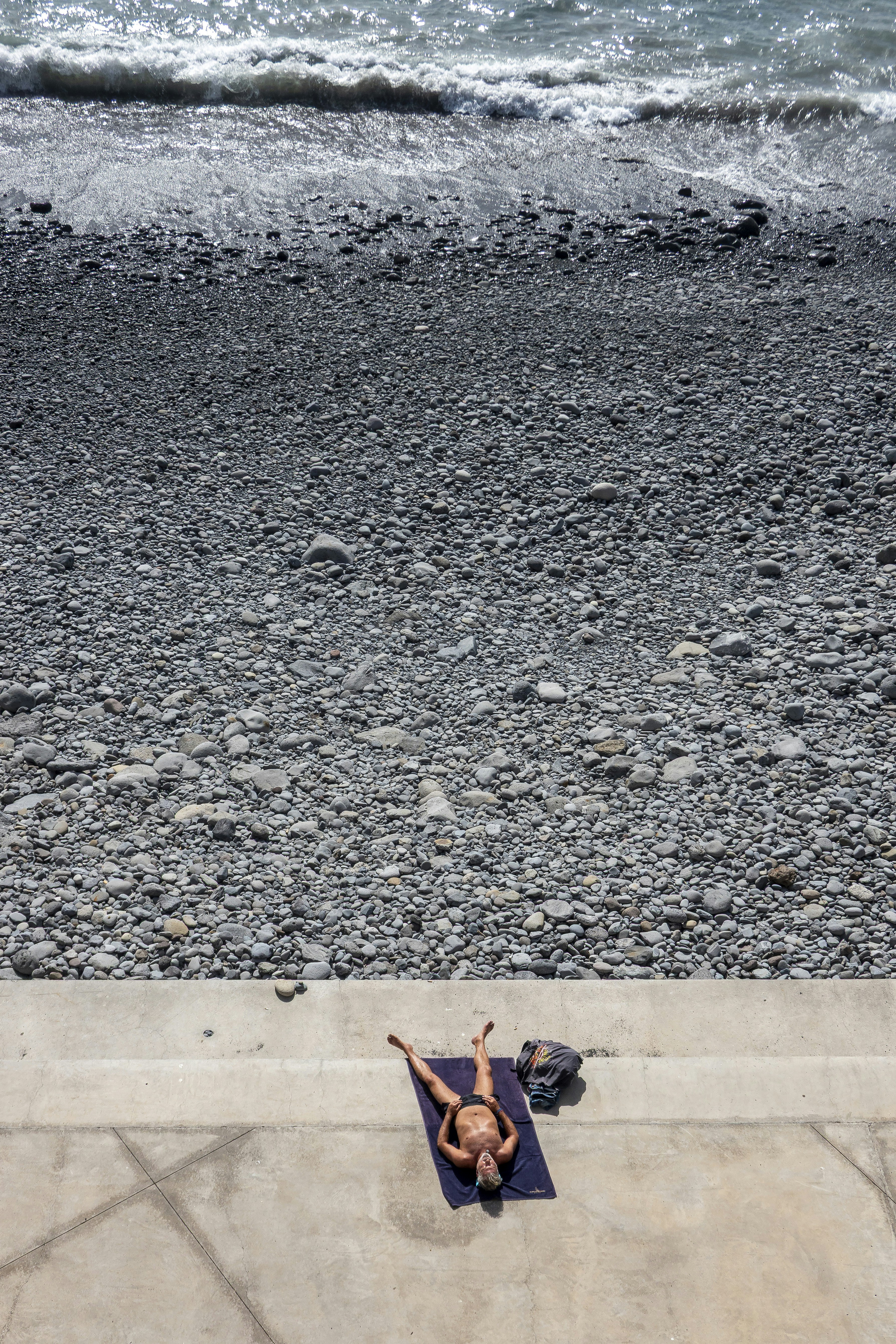 A person sunbathing on a pebble beach by the ocean.