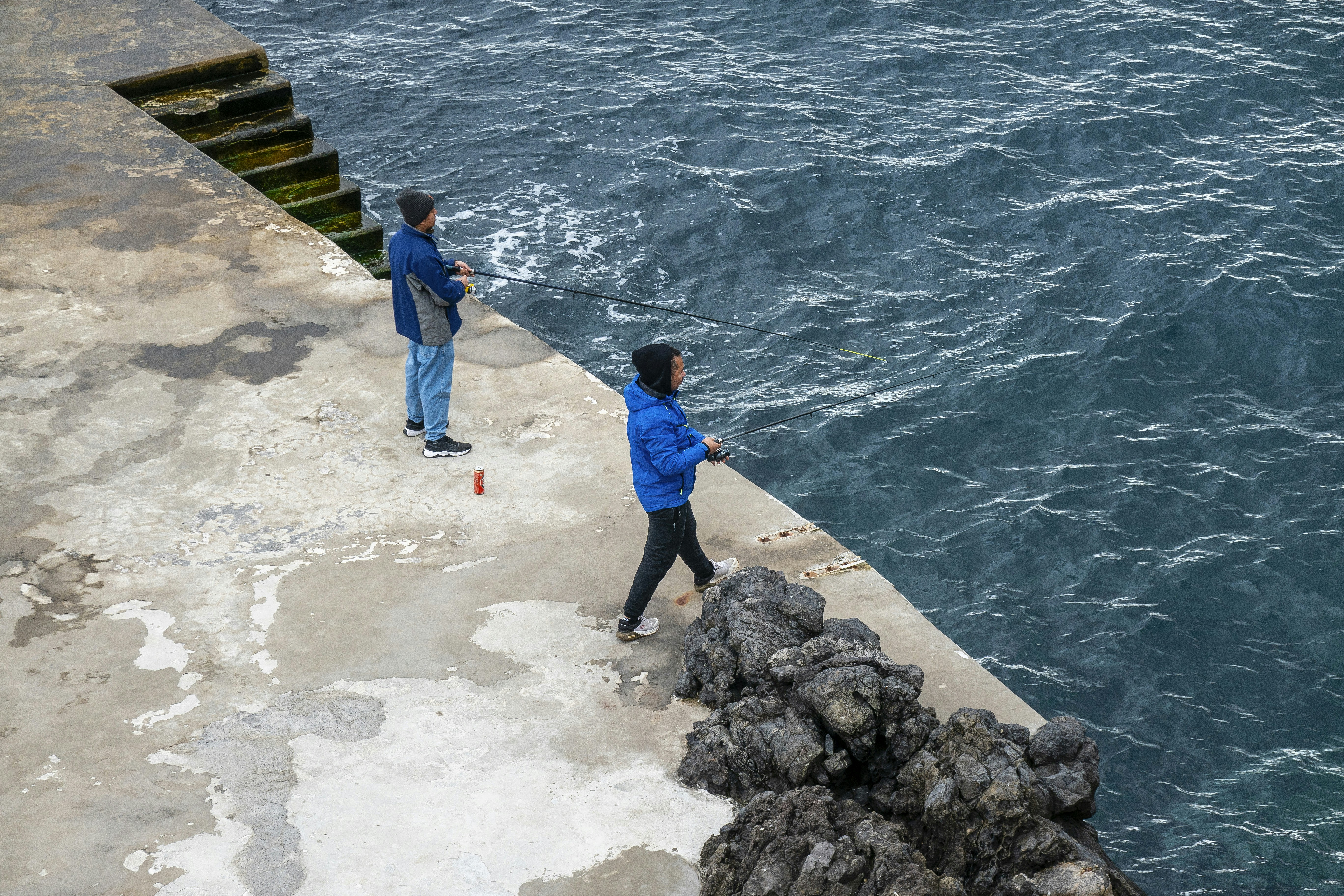 Two people fishing from a concrete pier