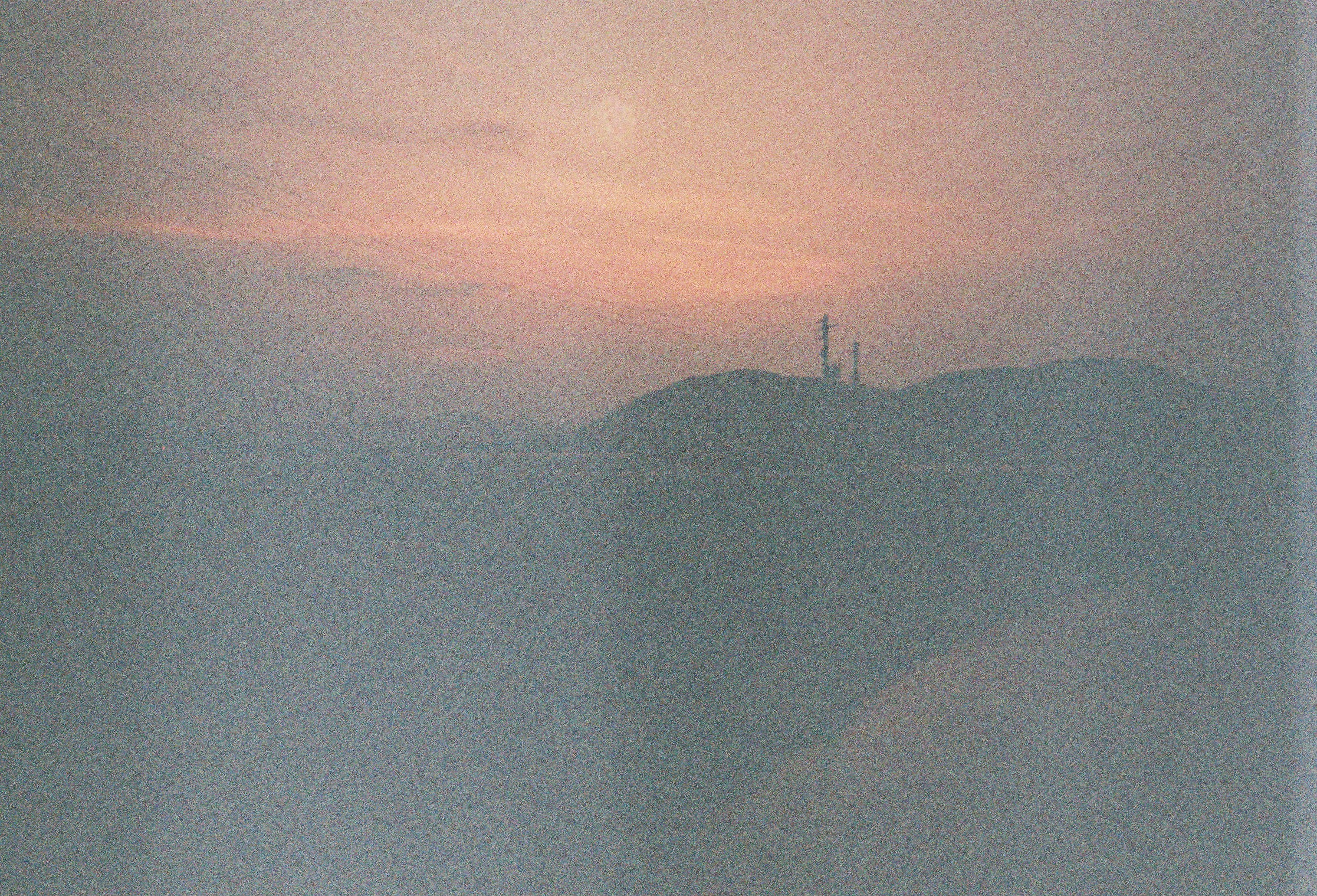 Pôr do sol enevoado sobre um topo de colina em silhueta, com torres.