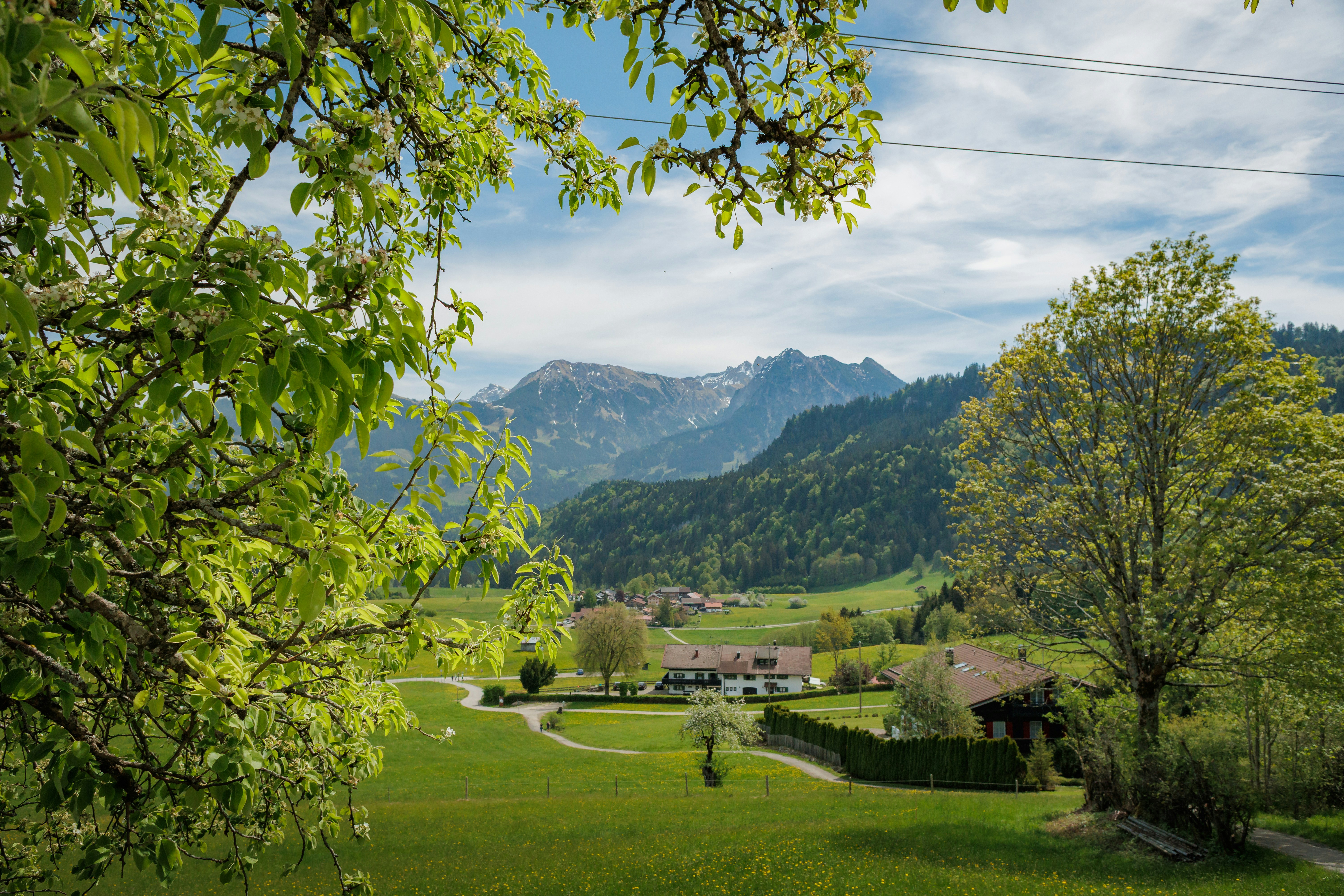 Valle verde con casas y montañas lejanas bajo un cielo azul