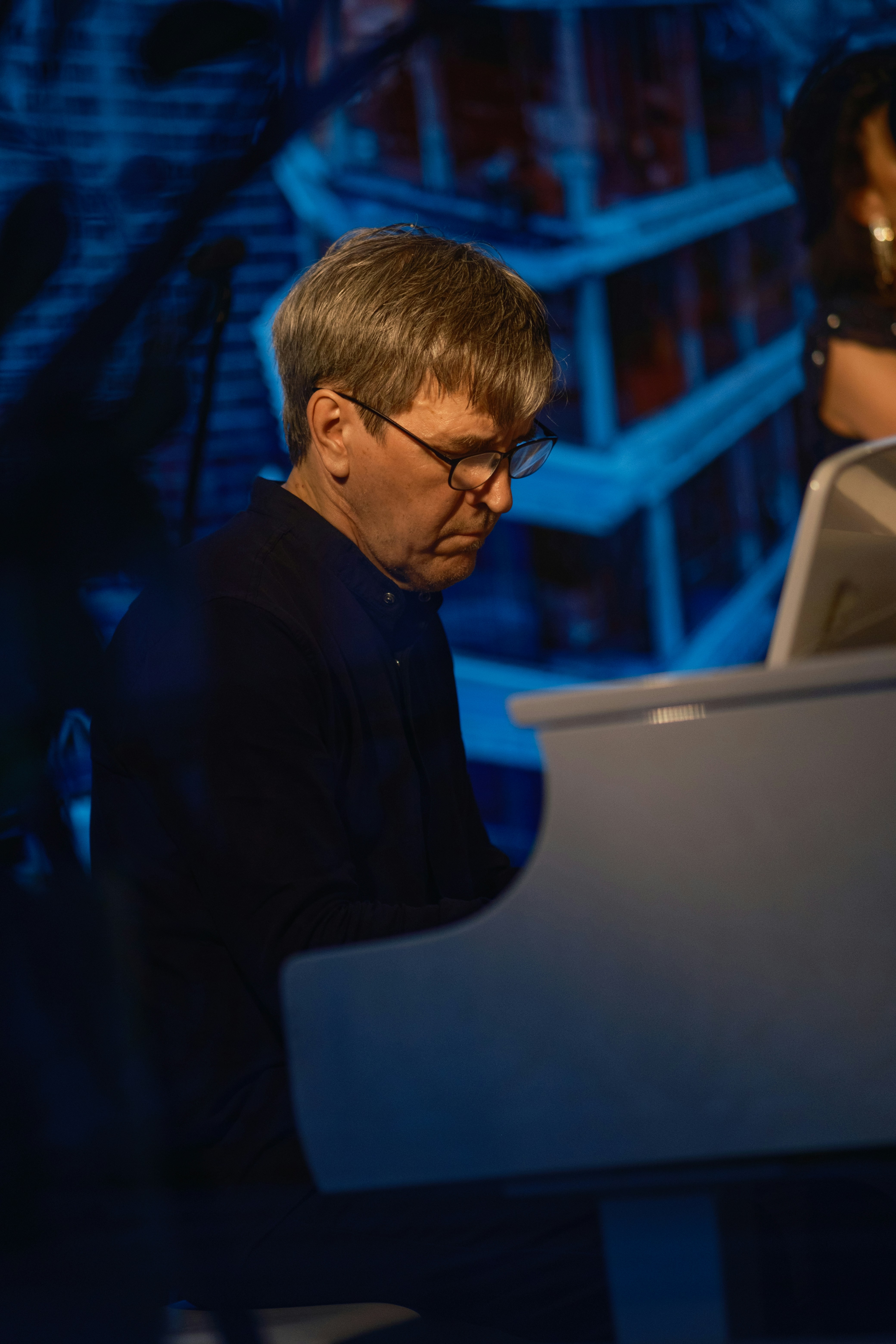 Man in glasses playing a white piano indoors.