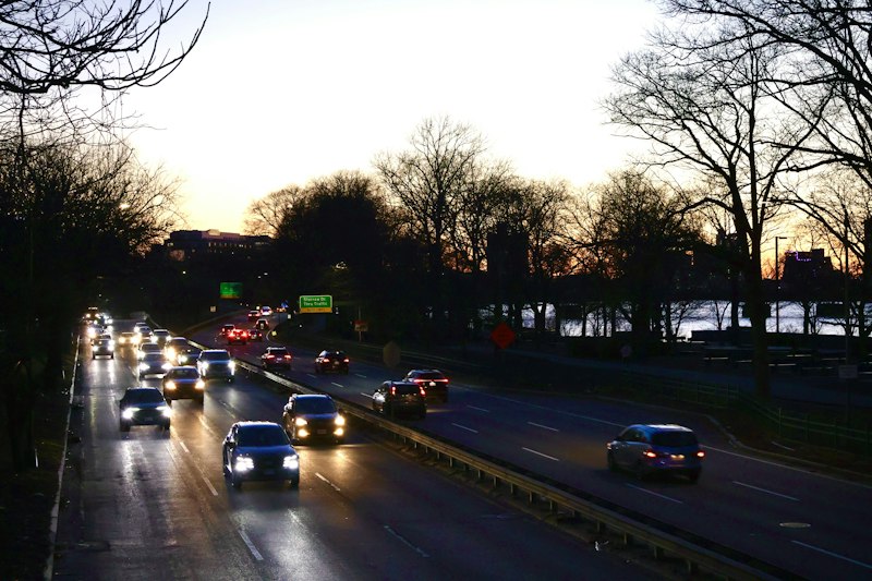 Headlights on a Boston riverside parkway at dusk, the drive home after a medical appointment in the city