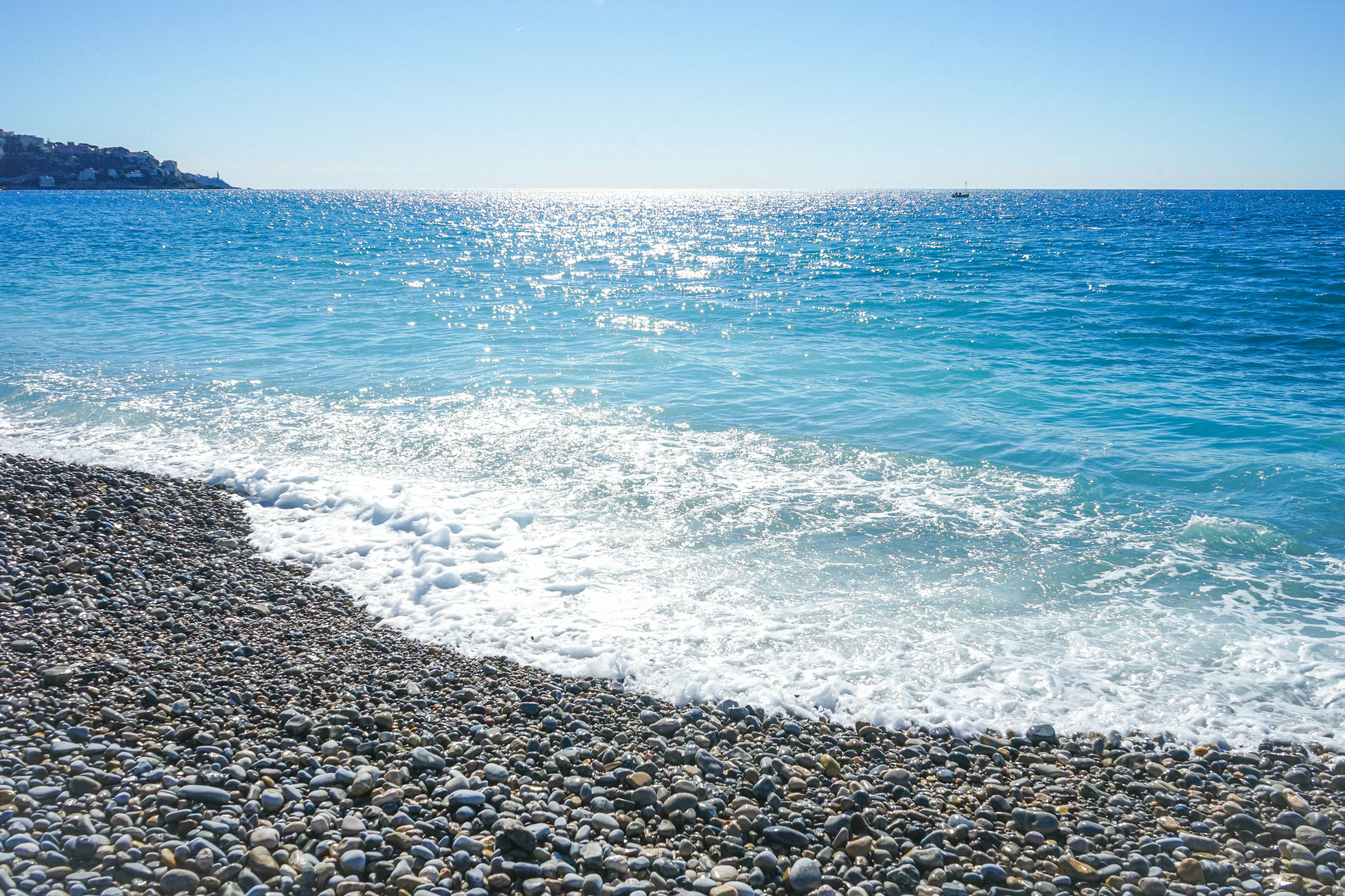Pebble beach with sparkling blue ocean waves under clear sky