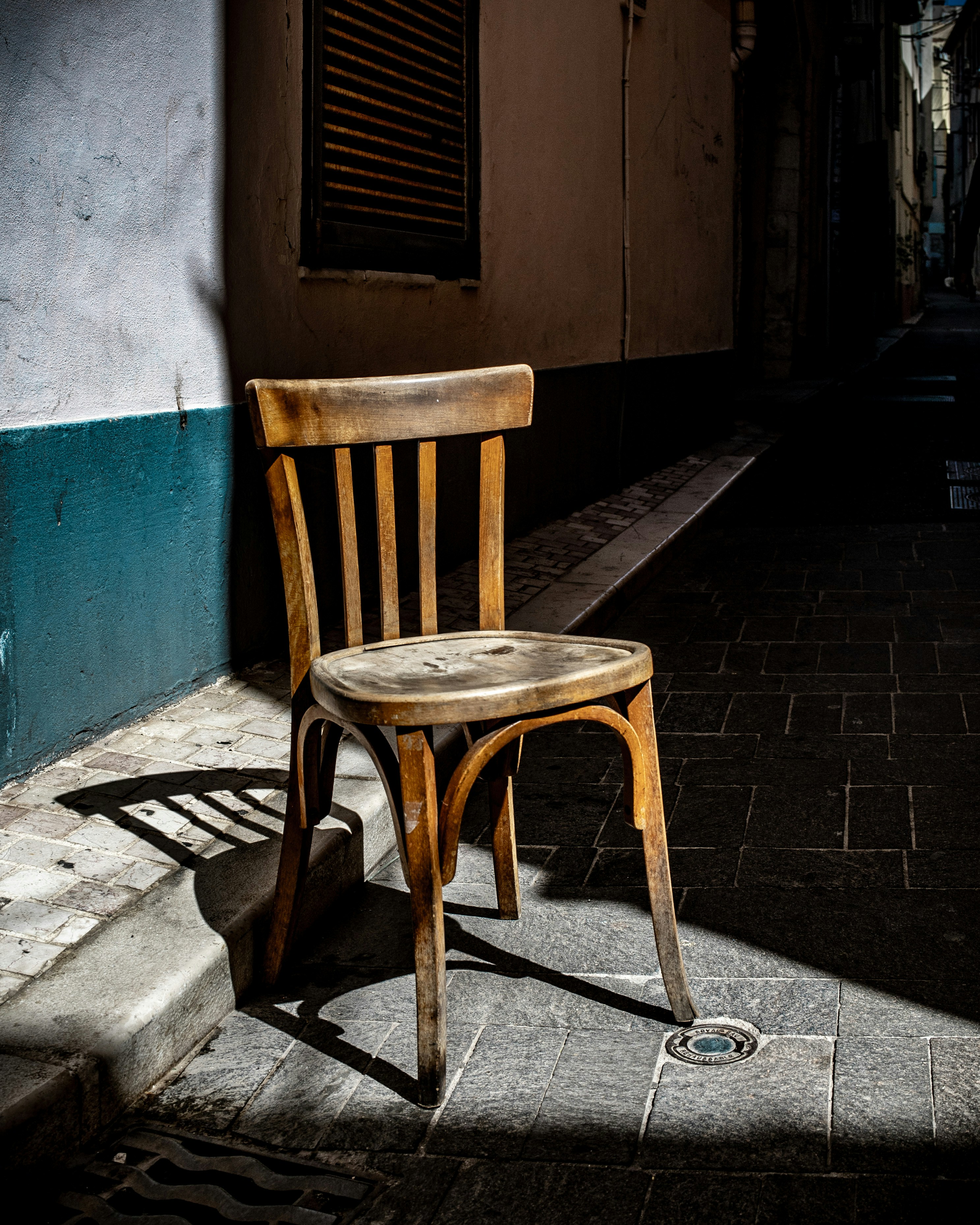 Uma velha cadeira de madeira está em um beco iluminado pelo sol.