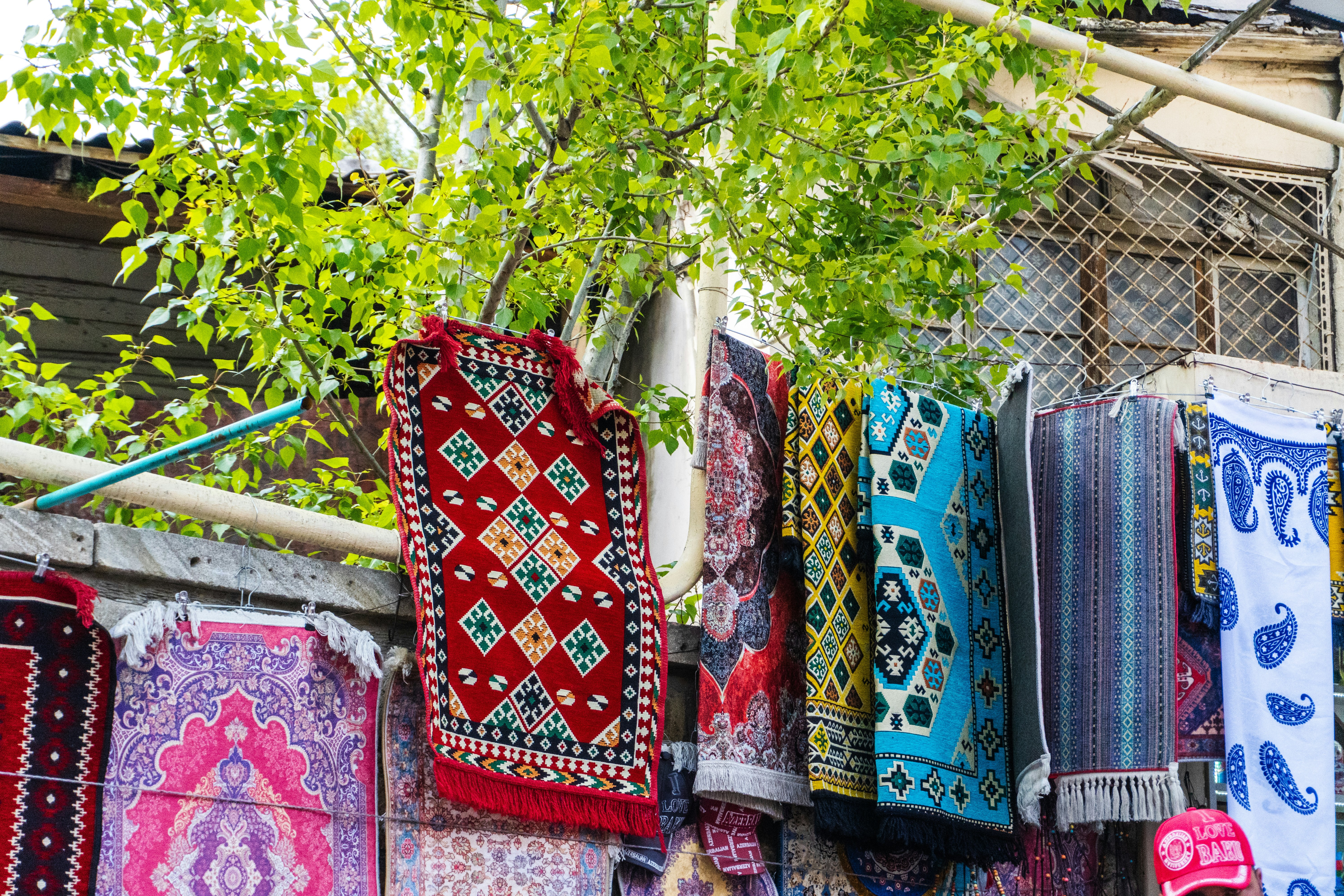 Colorful rugs and textiles displayed outdoors with greenery.