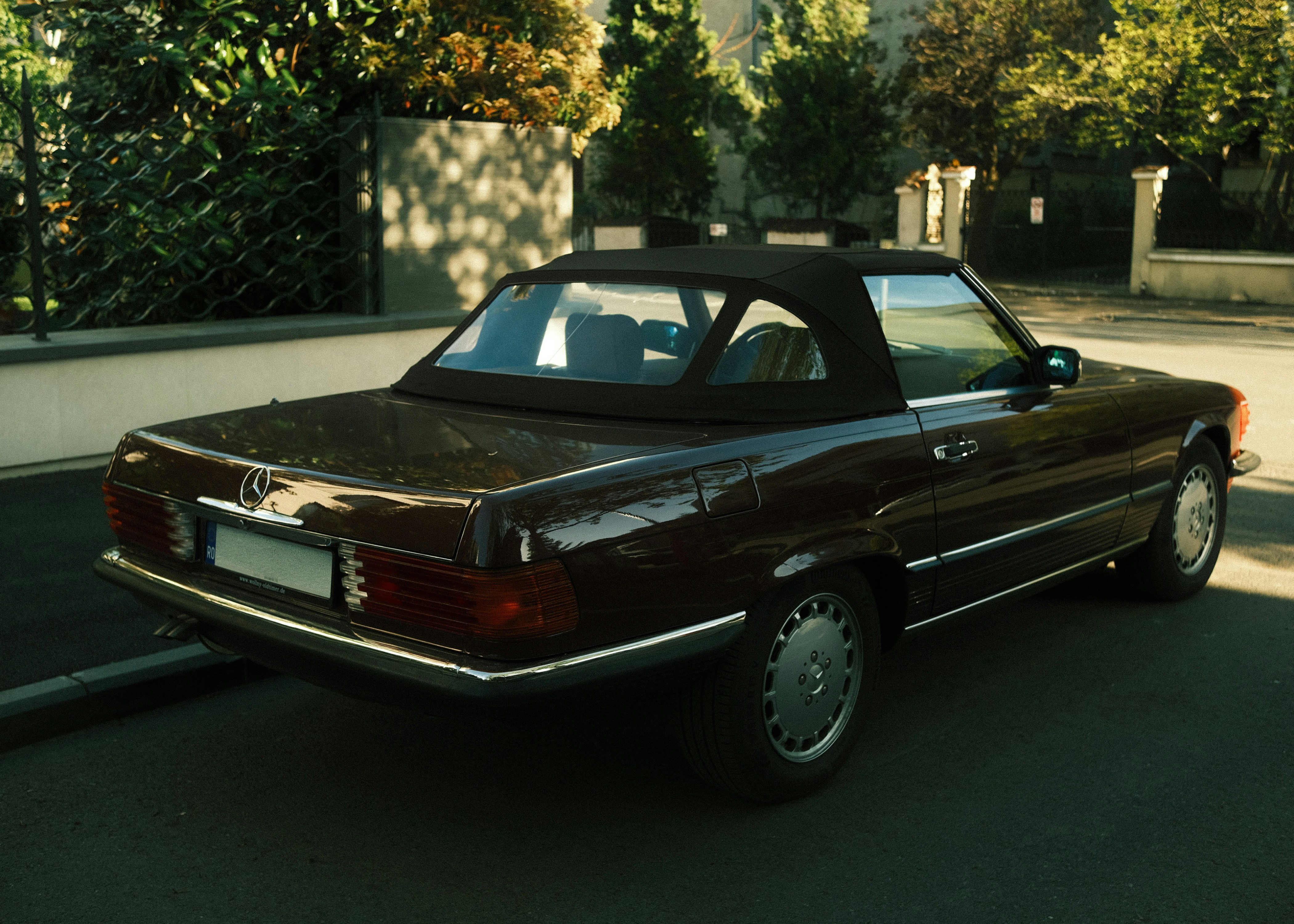 Burgundy Mercedes-Benz R107 SL roadster with its soft top up, rear three-quarter view