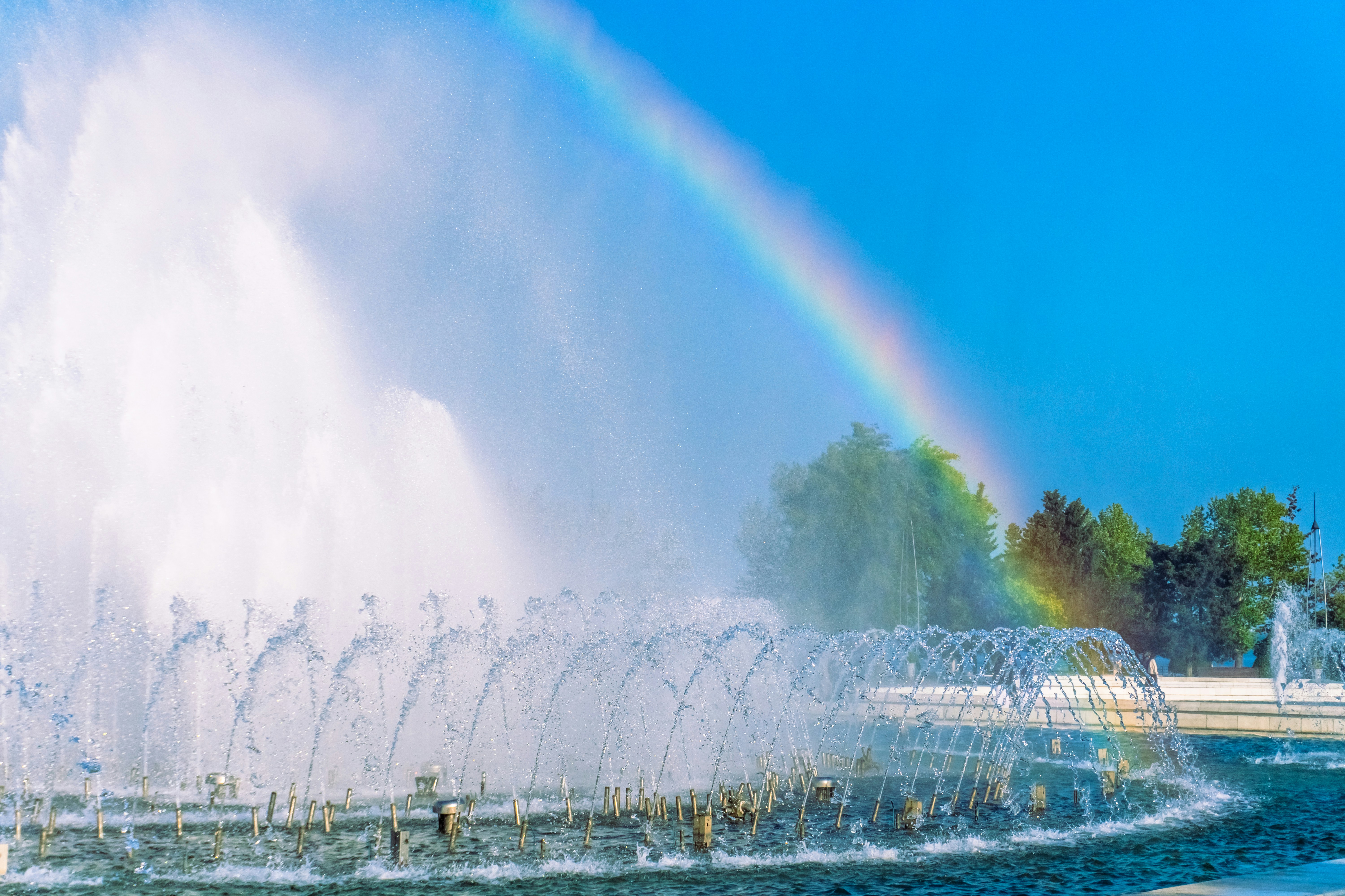A fountain sprays water creating a rainbow against blue sky.