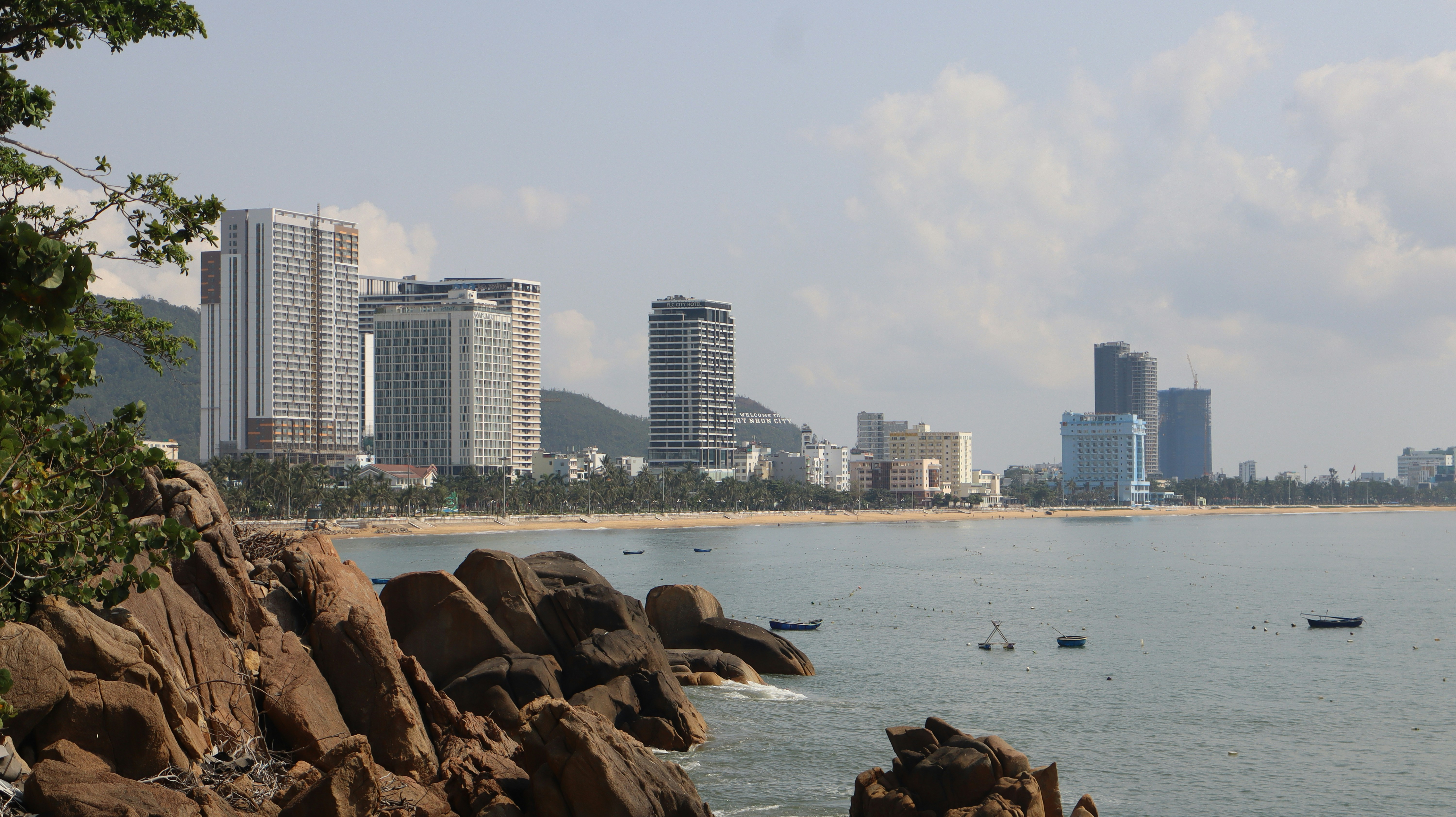 Coastal city skyline with rocky shore and calm ocean.