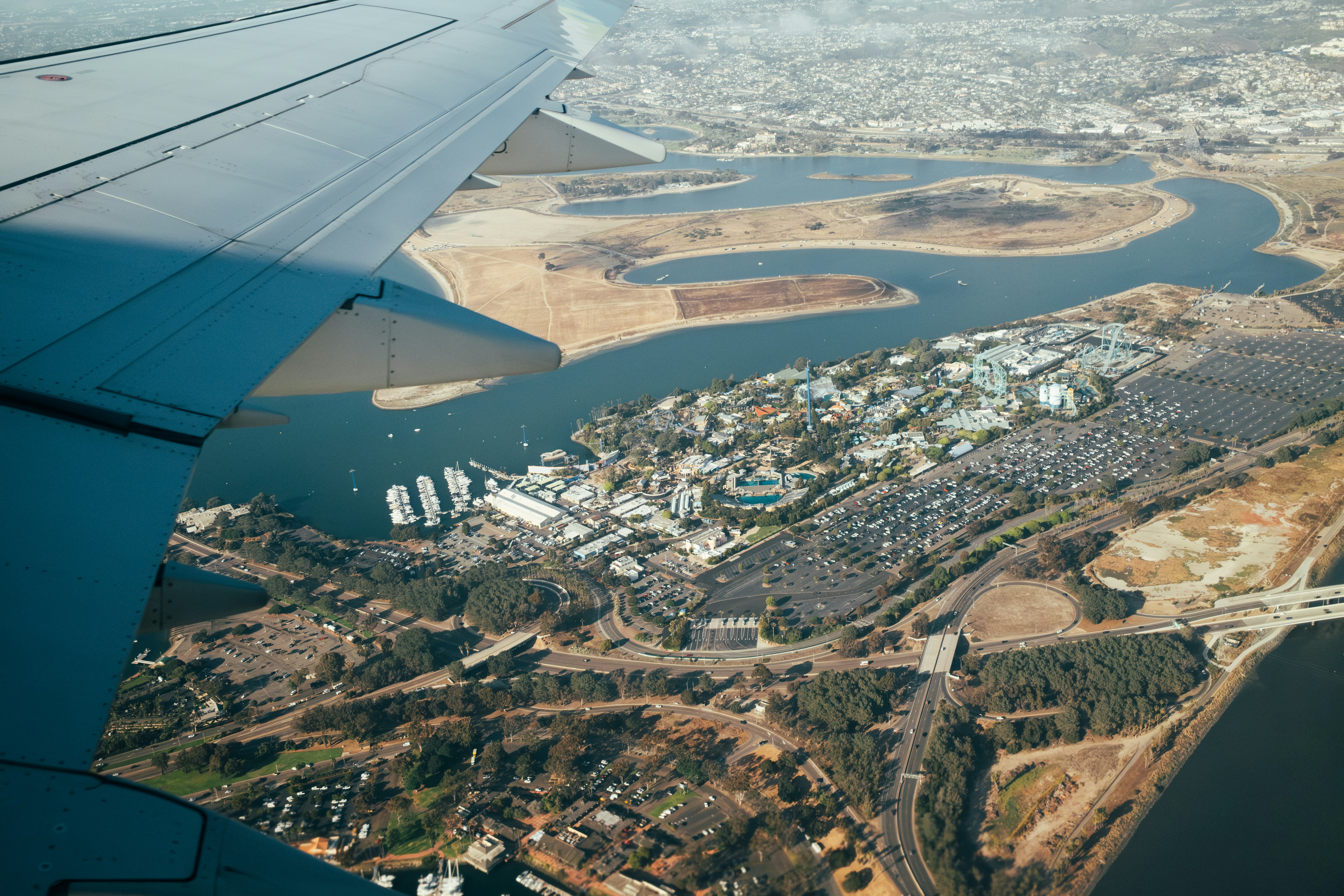 Airplane wing over coastal city with bay and harbor