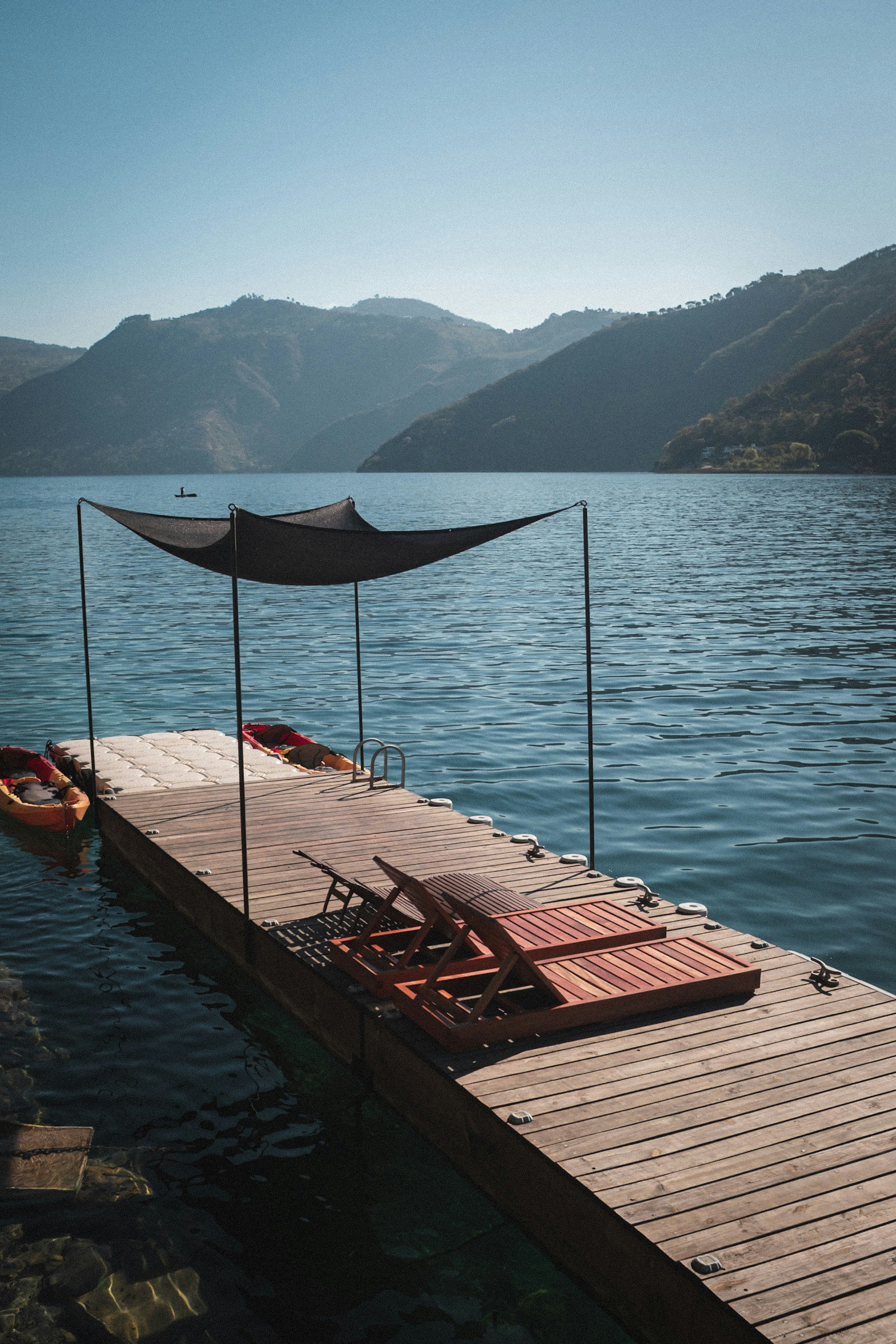Quai en bois avec chaises longues et kayaks sur un lac.