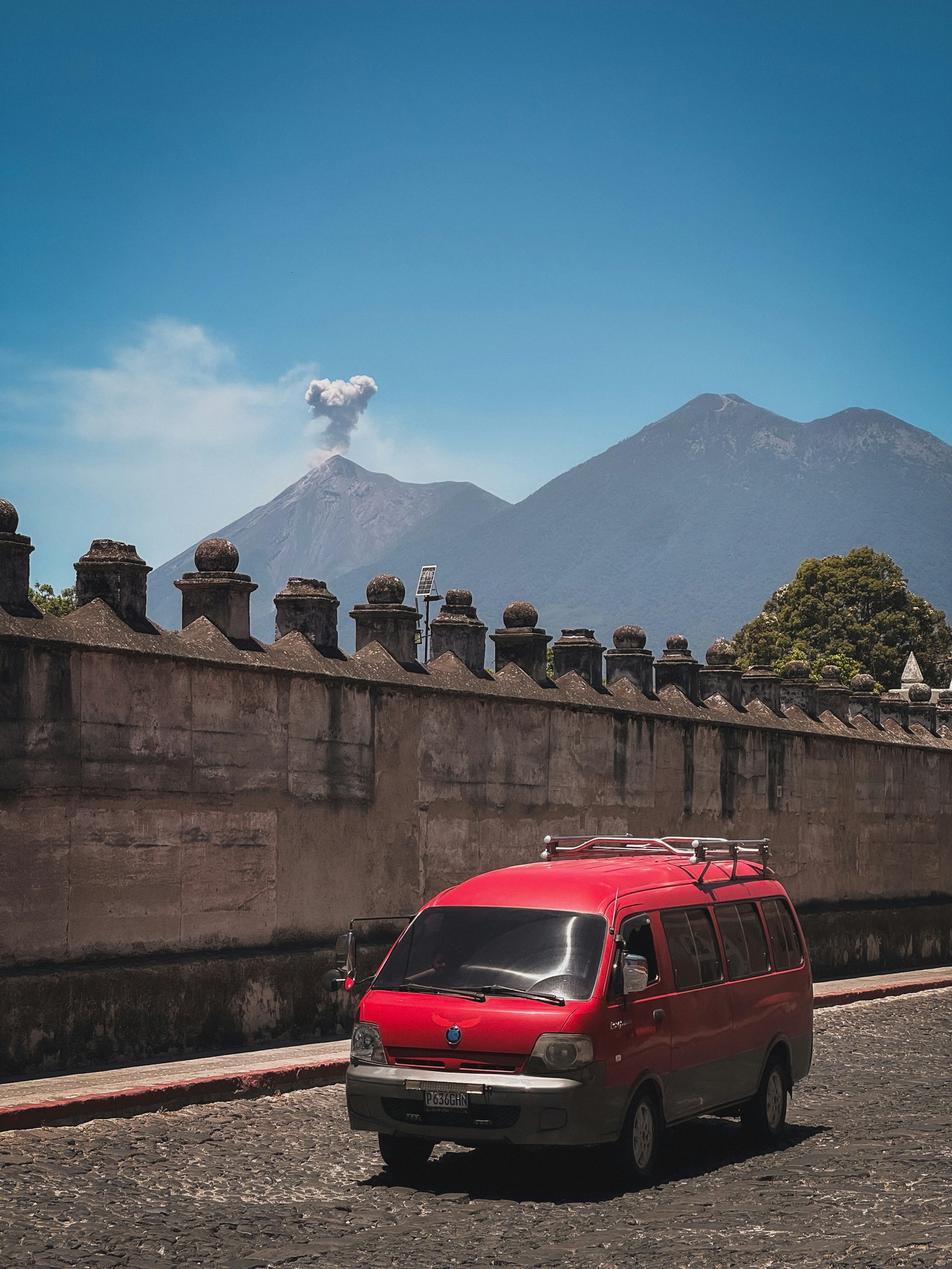Fourgonnette rouge sur une rue pavée avec un volcan fumant derrière