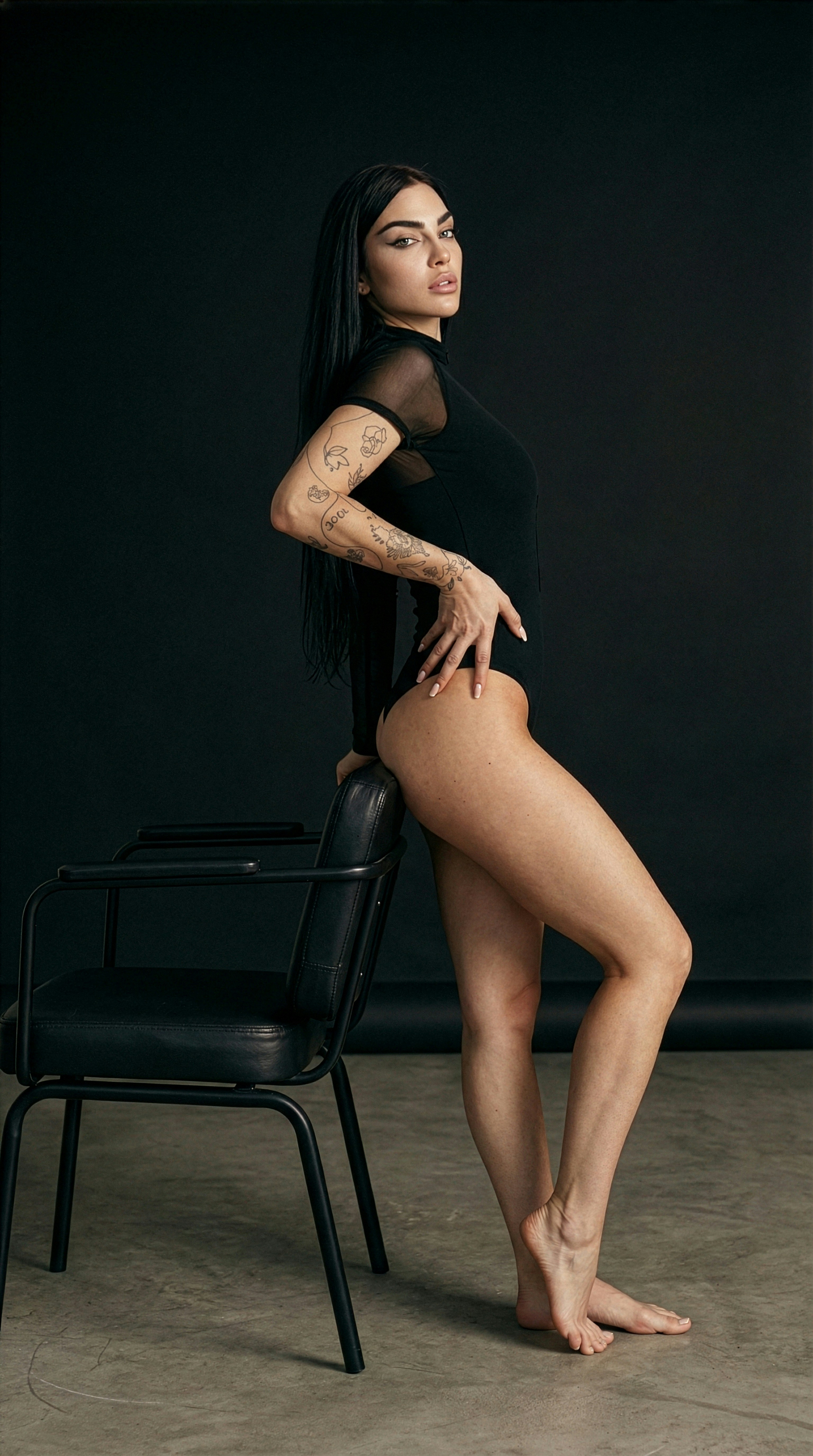 Woman in black bodysuit leans on chair