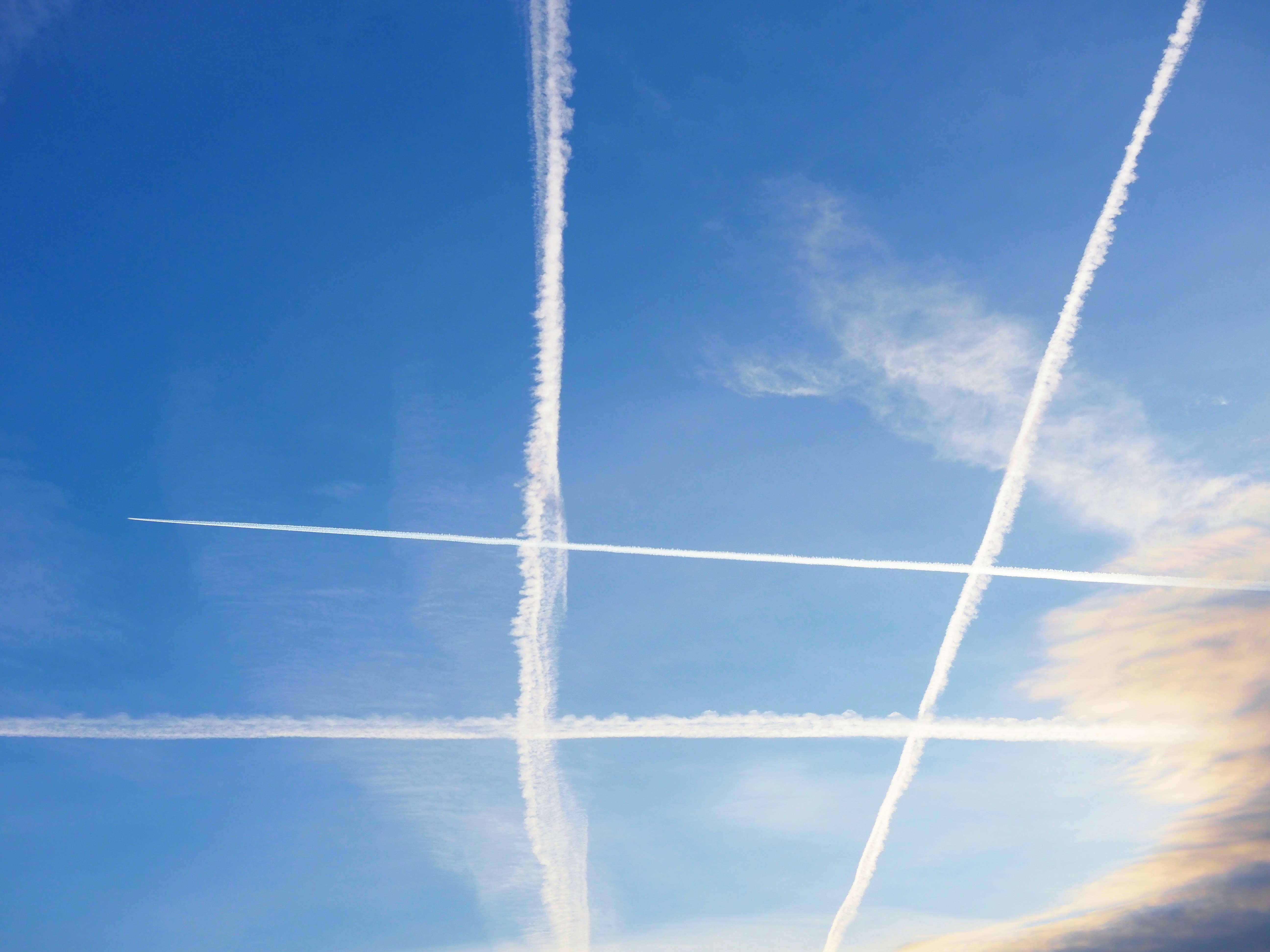 Multiple airplane contrails crisscross a bright blue sky.