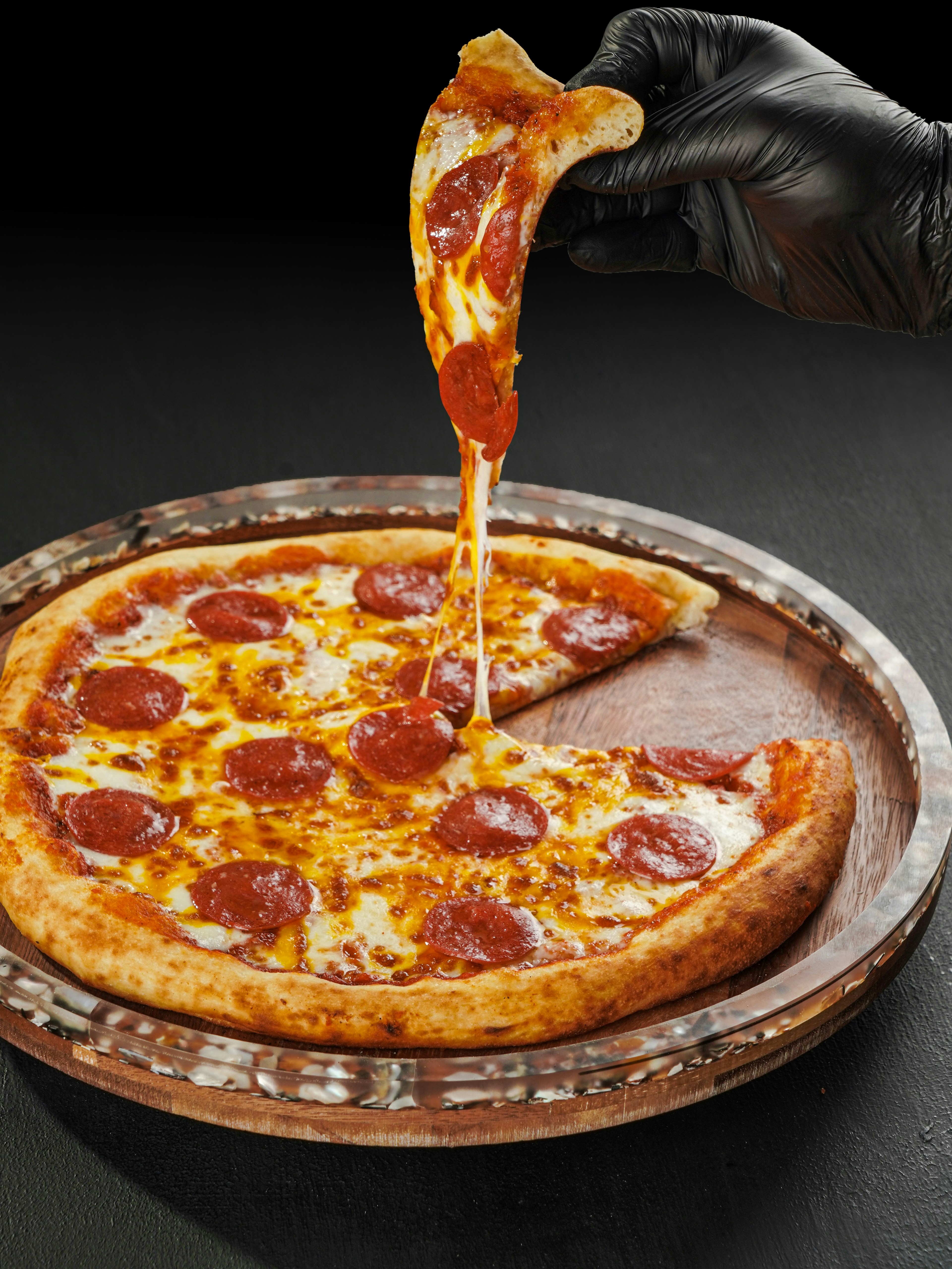 Hand lifting slice of pepperoni pizza with cheese pull