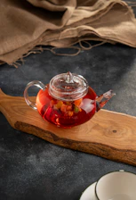 Glass teapot filled with red fruit tea and fruit pieces.