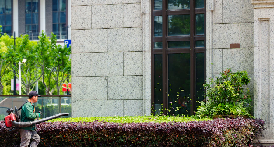 Gardener clearing leaves near shrubs outside a building