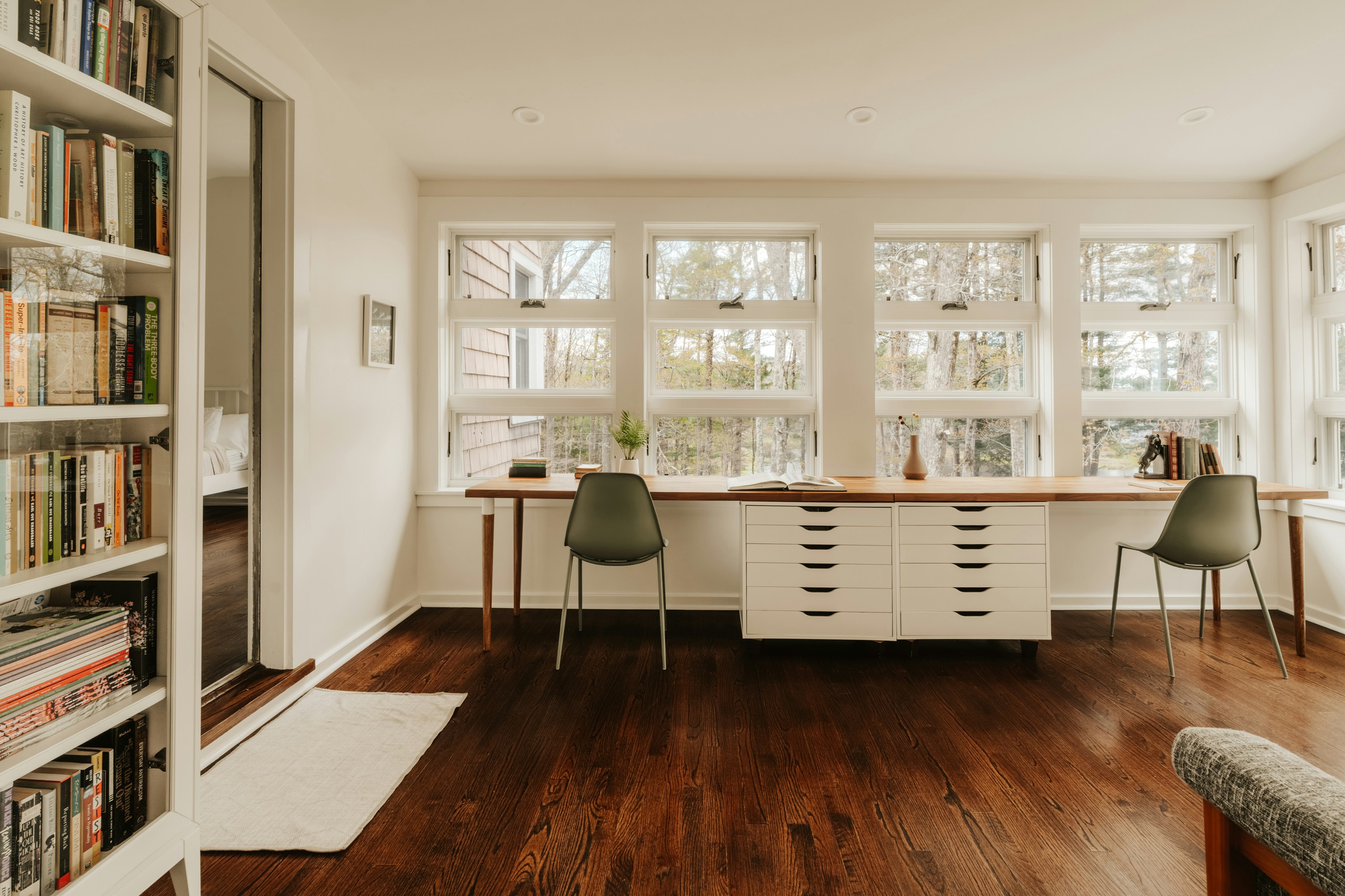 Bright room with bookshelves and two desks by windows.