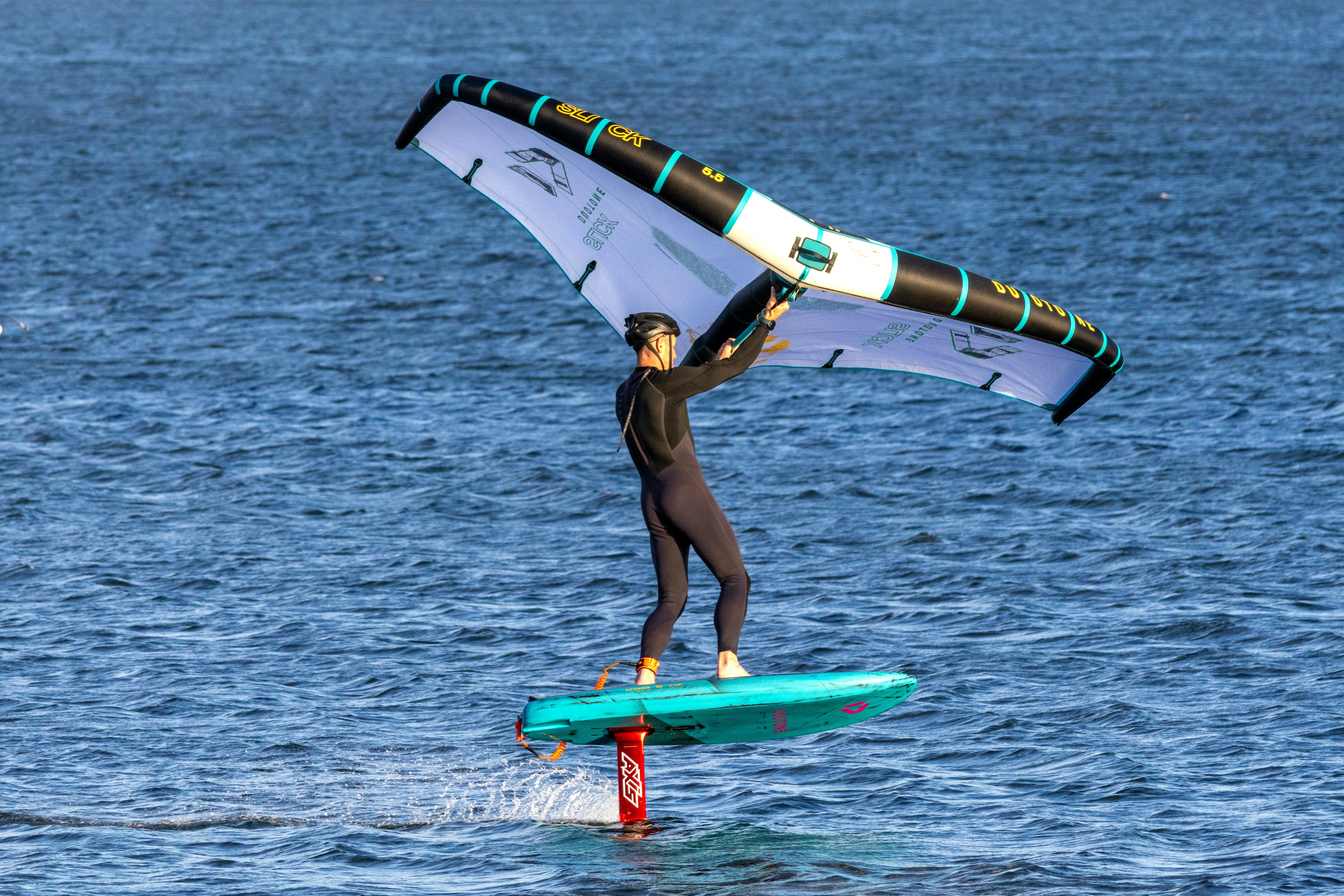 Person wing foiling on a turquoise board over blue water