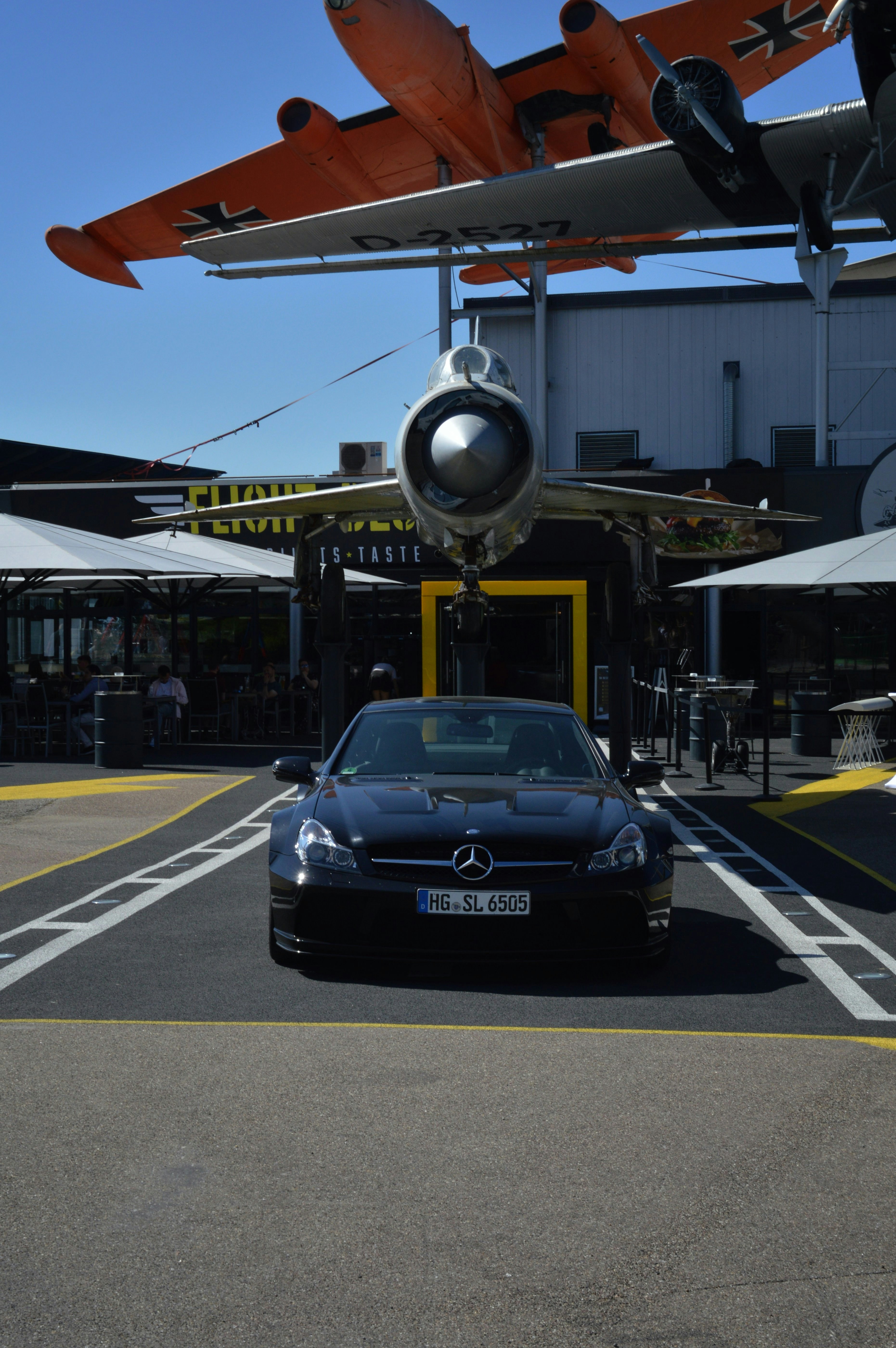Black mercedes-benz parked under two airplanes