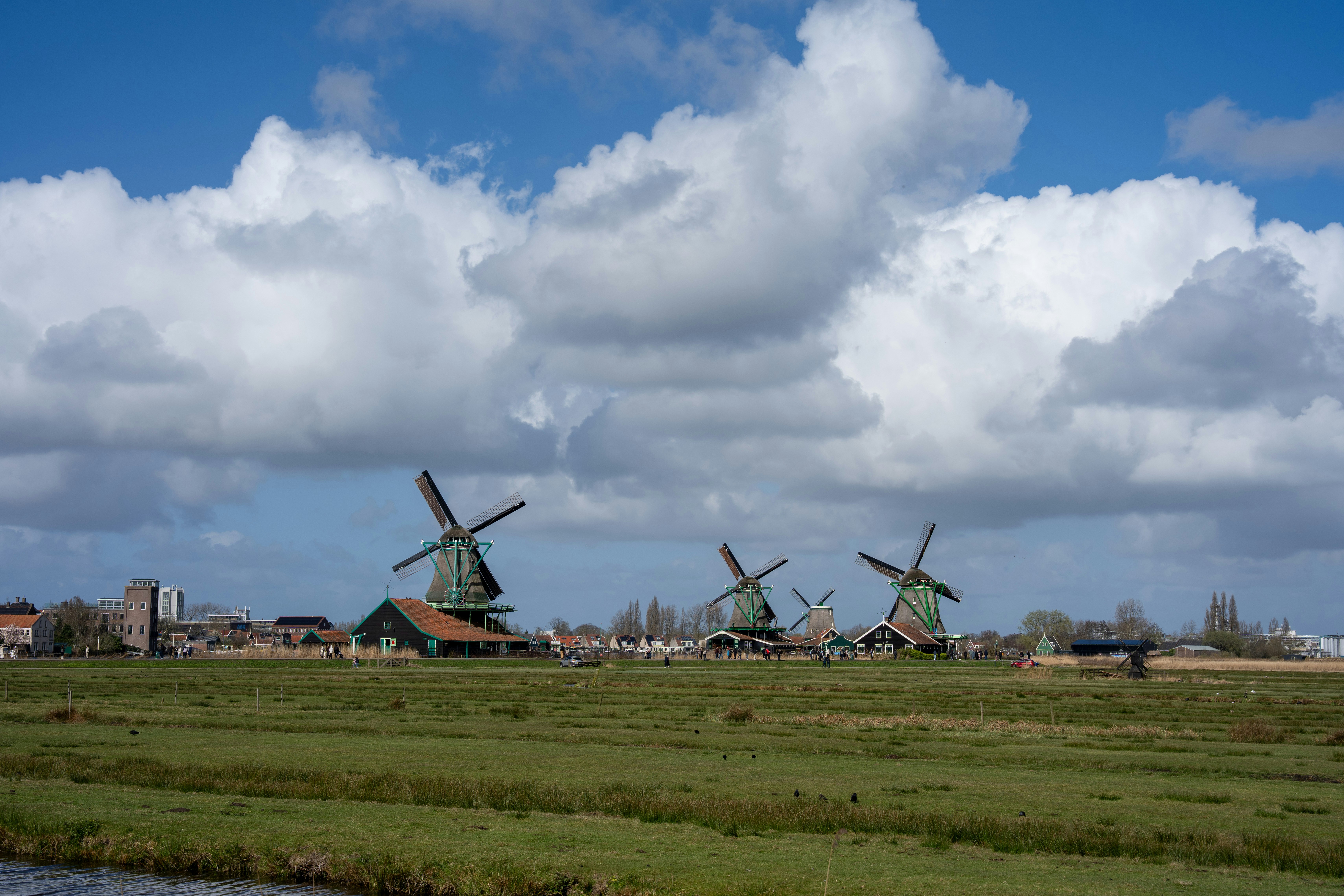 Three windmills stand in a green field under clouds.