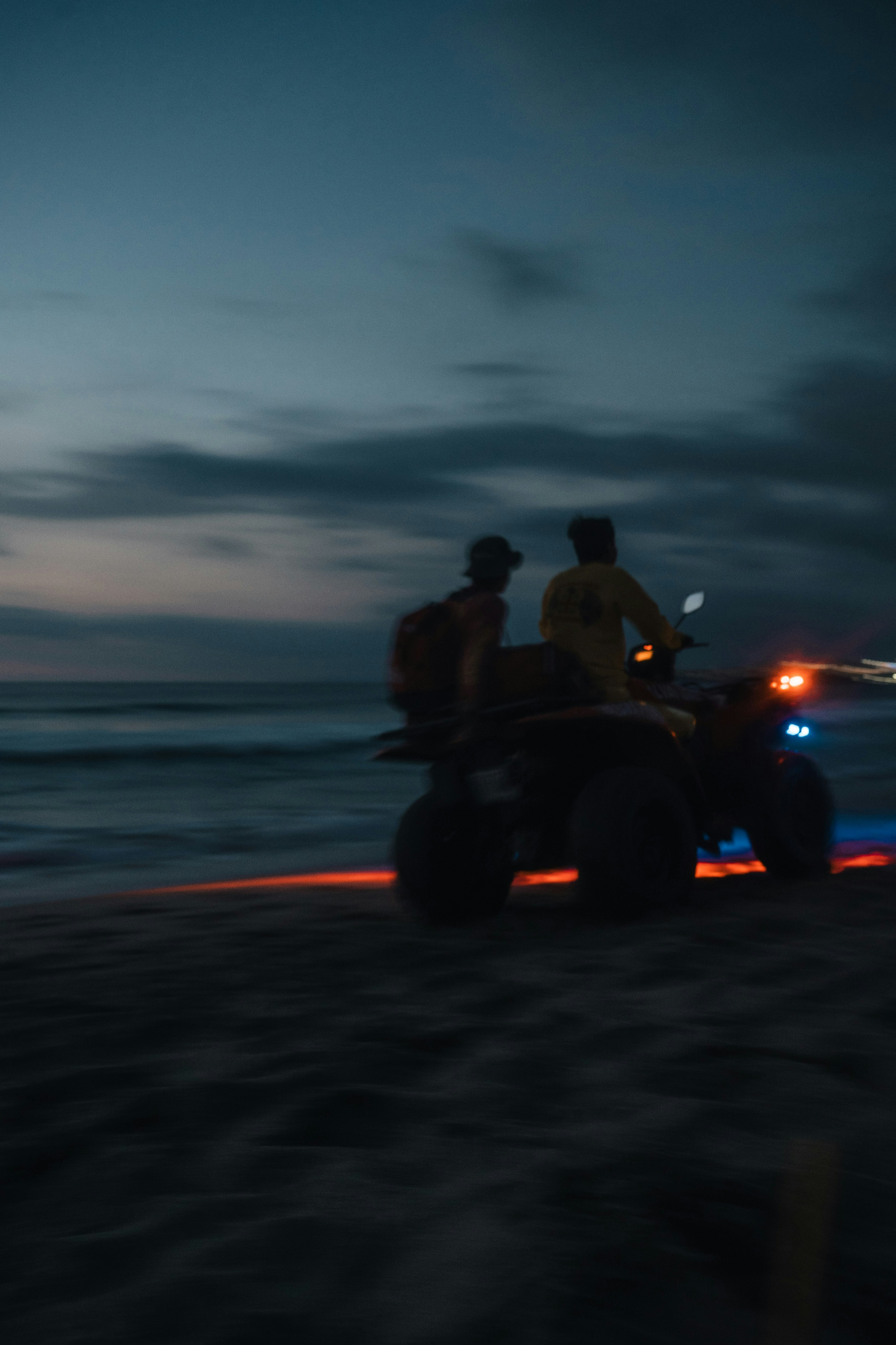 Two people on an atv on a beach at dusk.