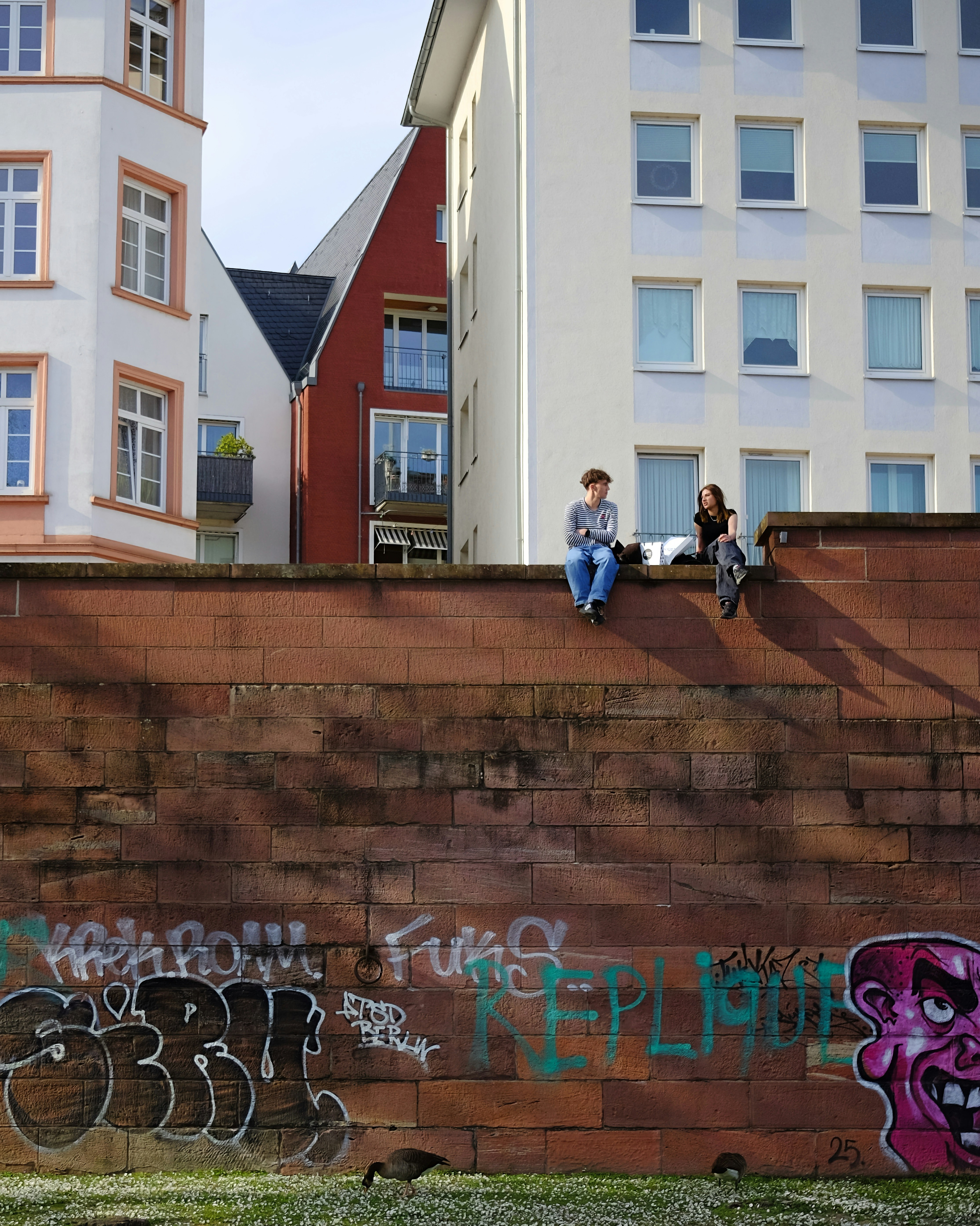 Drei Personen sitzen auf einer Backsteinwand mit Graffiti.