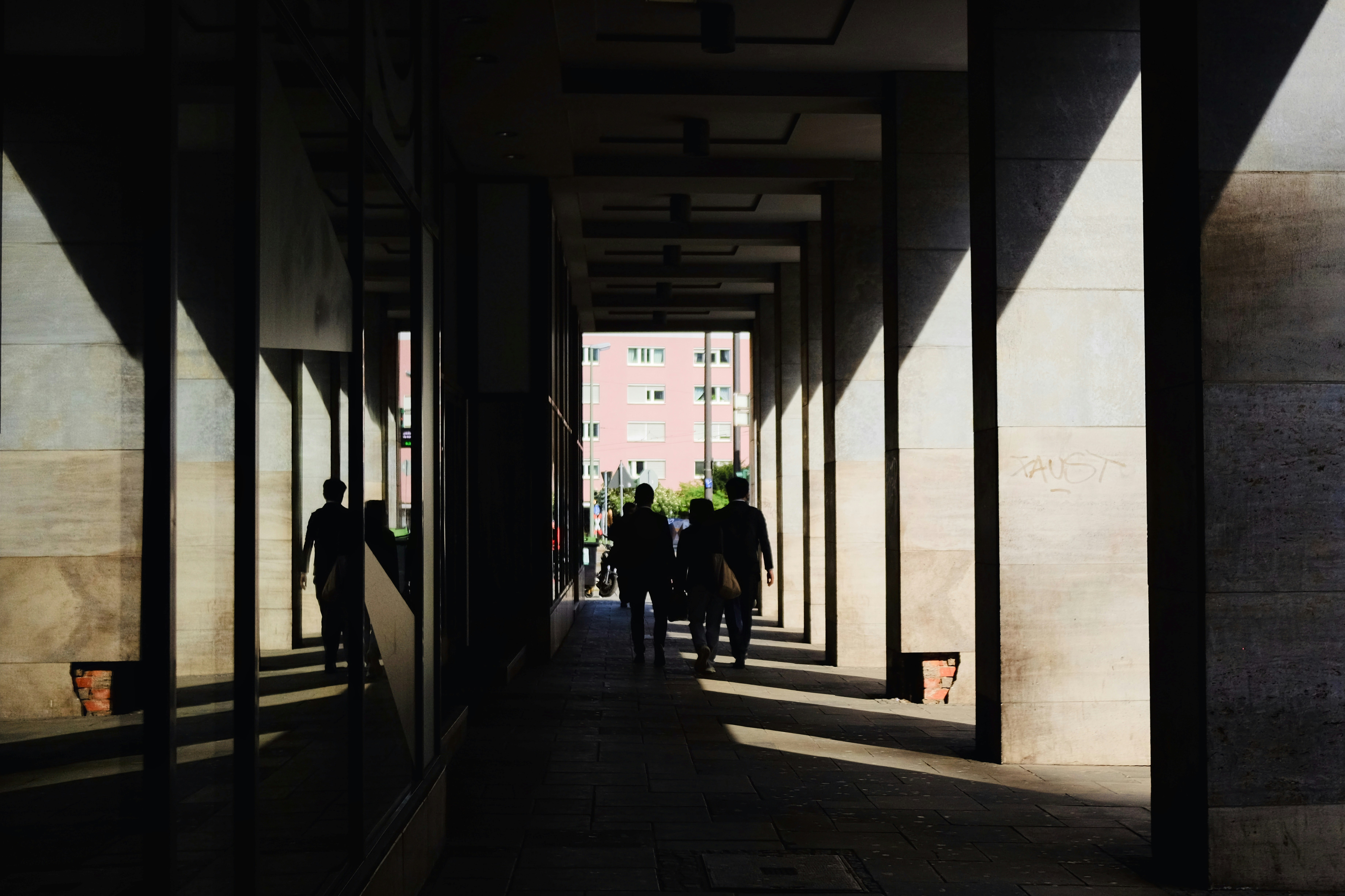Silhouetten von Menschen, die durch eine sonnenbeschienene Kolonnade gehen.
