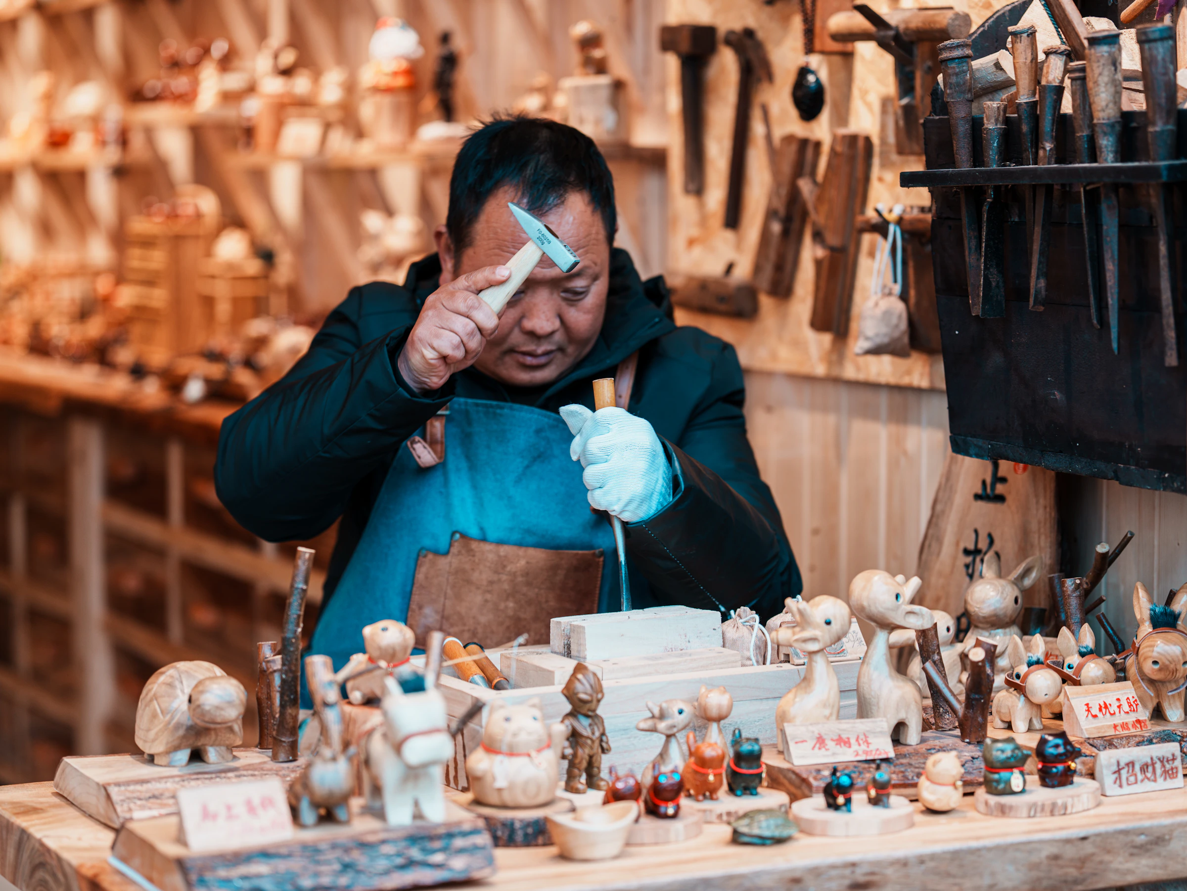 A woodcarver at his bench in a Chinese old-town workshop, his hand-carved figures laid out in front of him