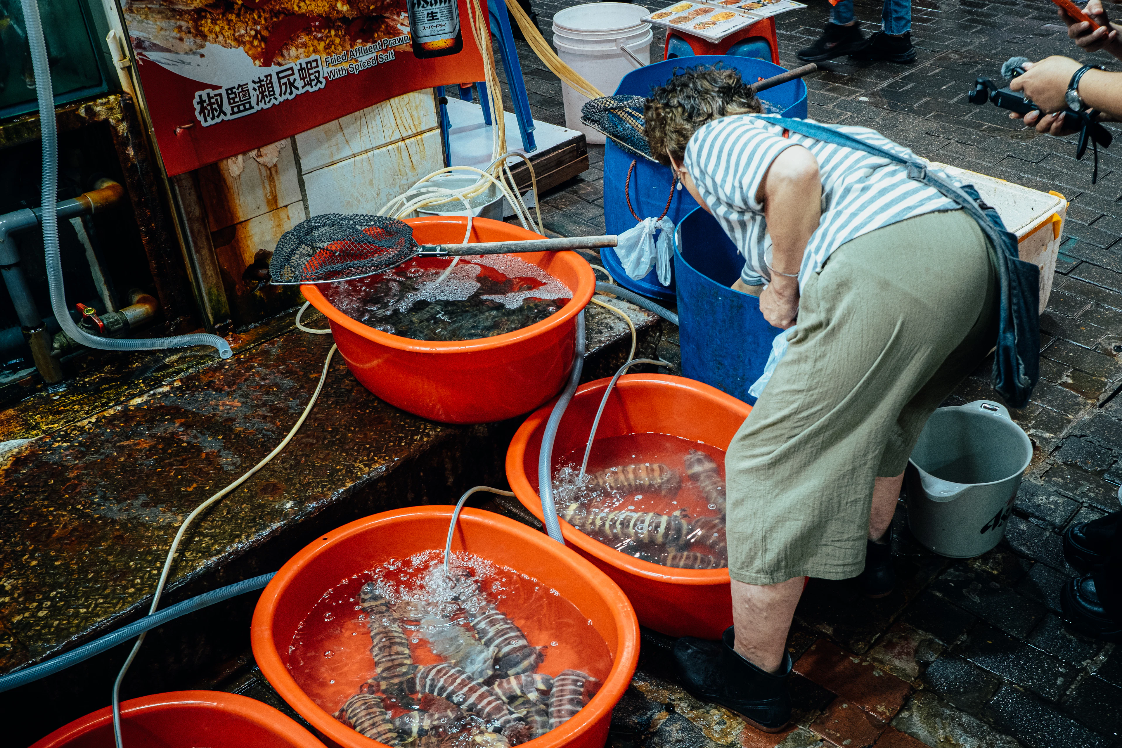 A fishmonger tending live seafood in orange tubs at a Hong Kong street market