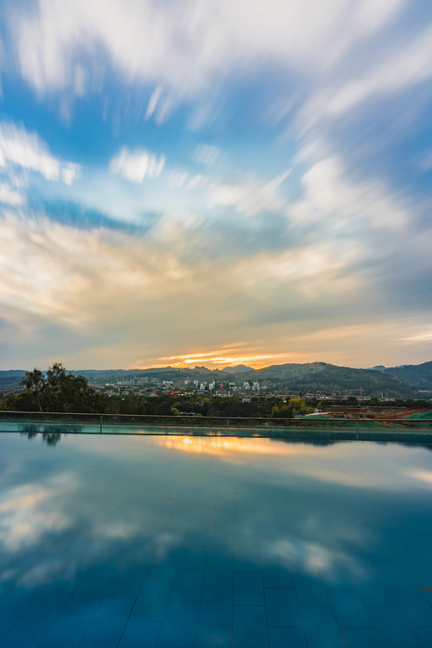 Calm swimming pool reflecting streaked clouds at sunset