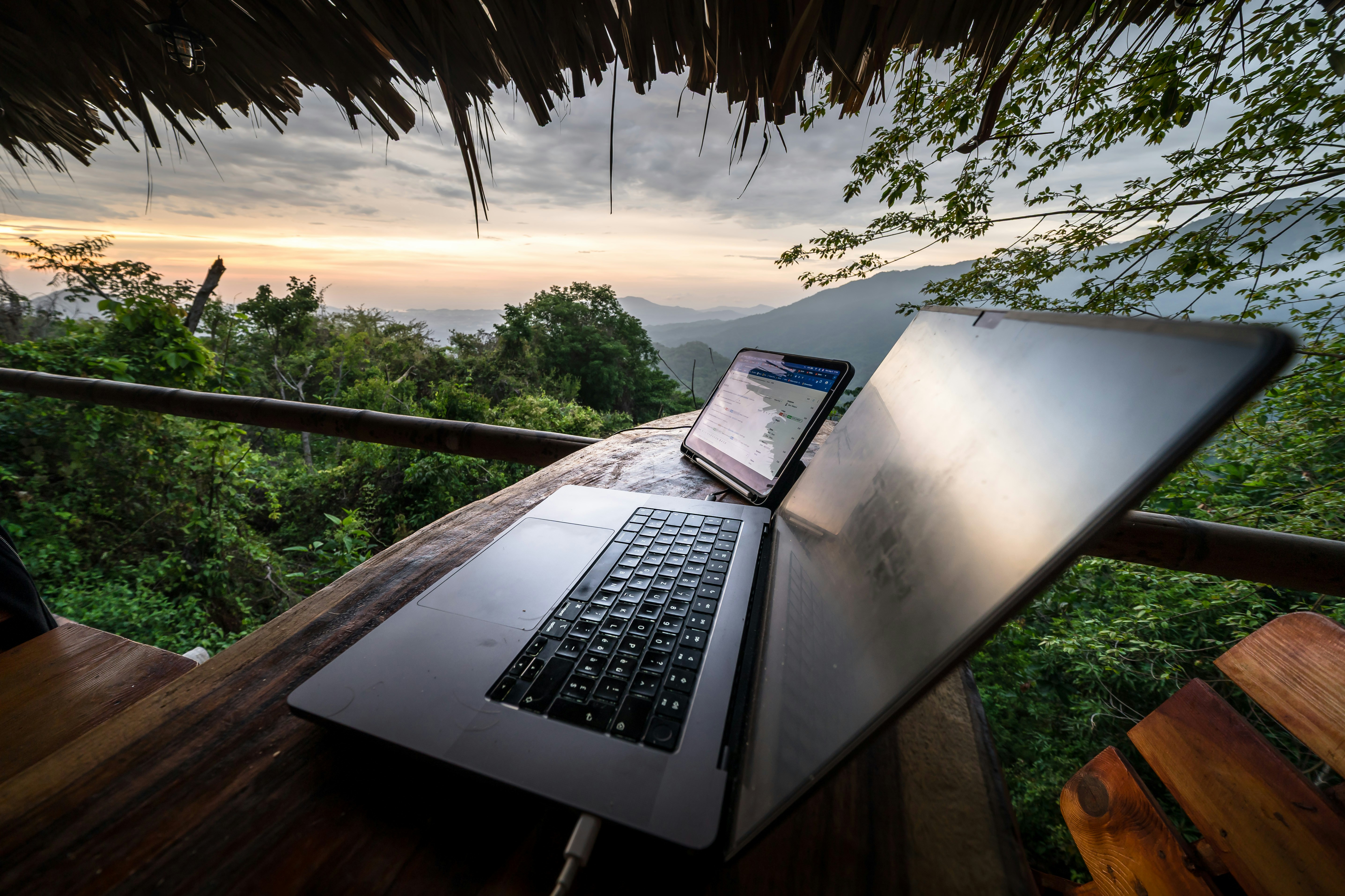 Laptop and phone on a wooden table with mountain view.