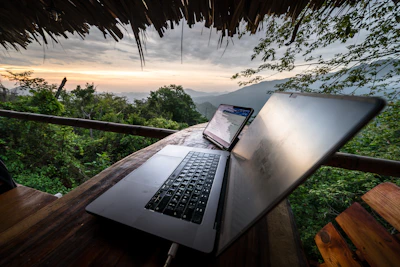 Laptop and phone on a wooden table with mountain view.