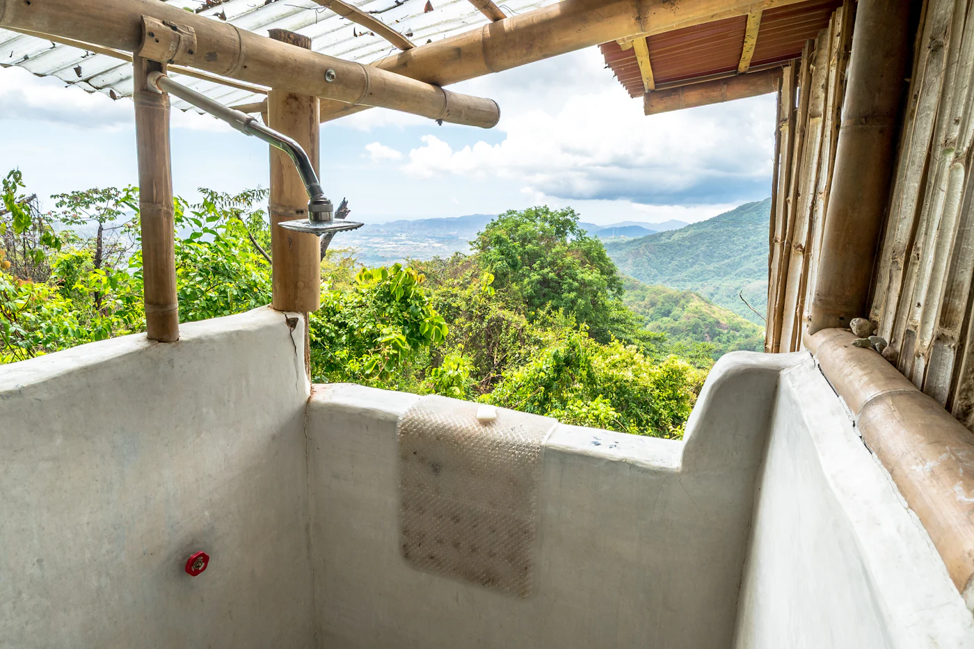 An open-air shower framed in bamboo, looking out to green hills