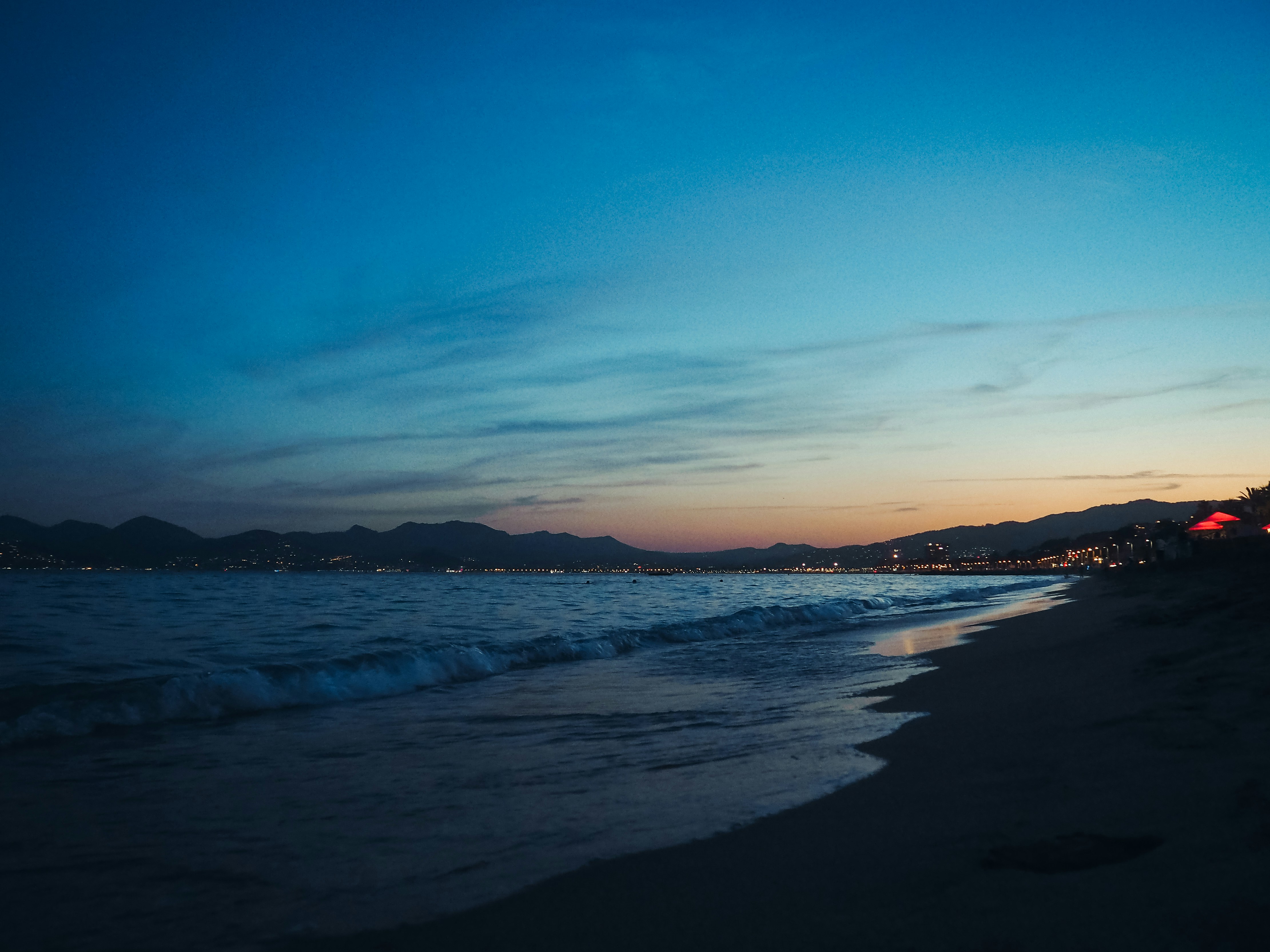 Ocean waves lap a dark sandy beach at dusk.