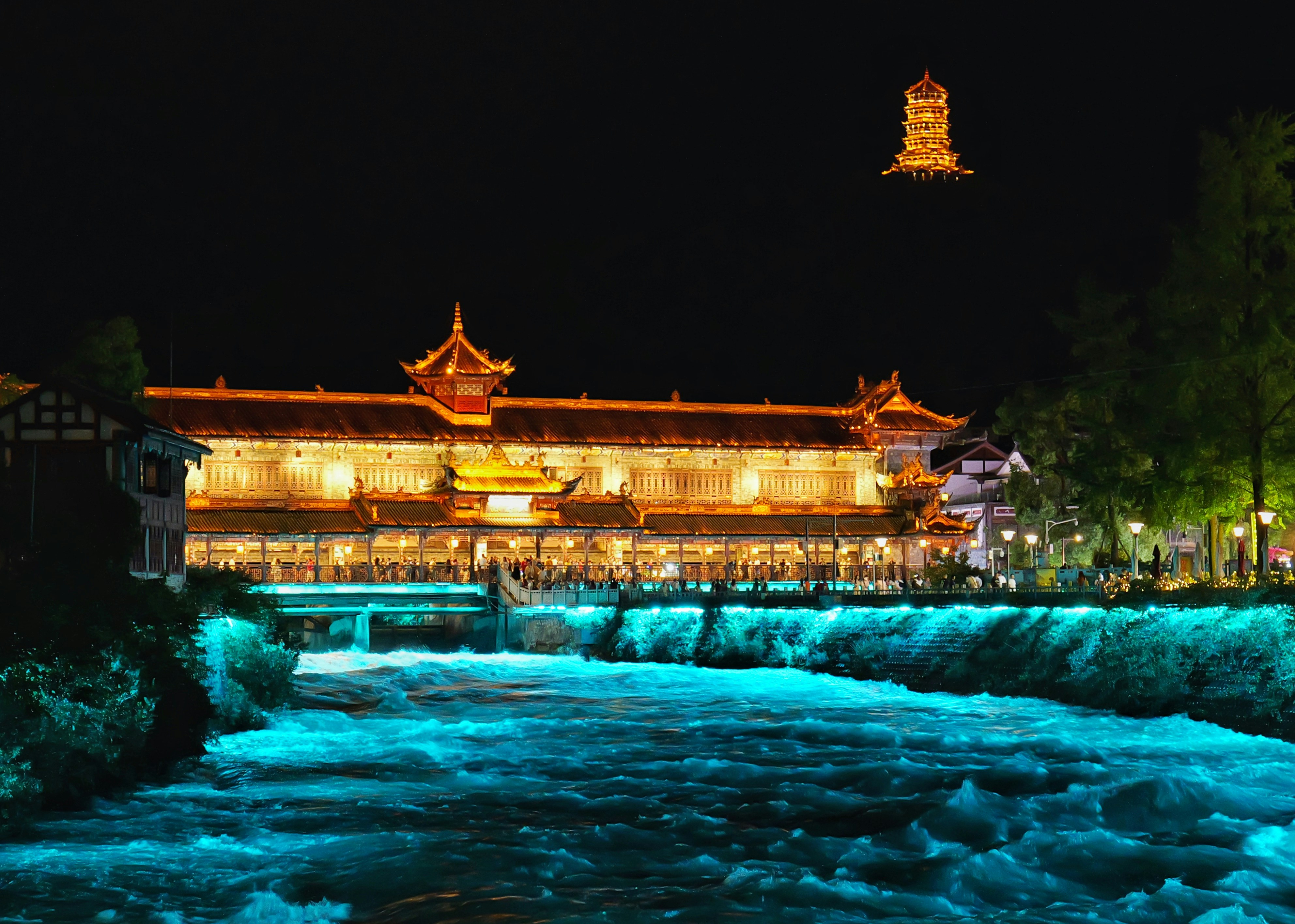 Illuminated building beside a glowing river at night.
