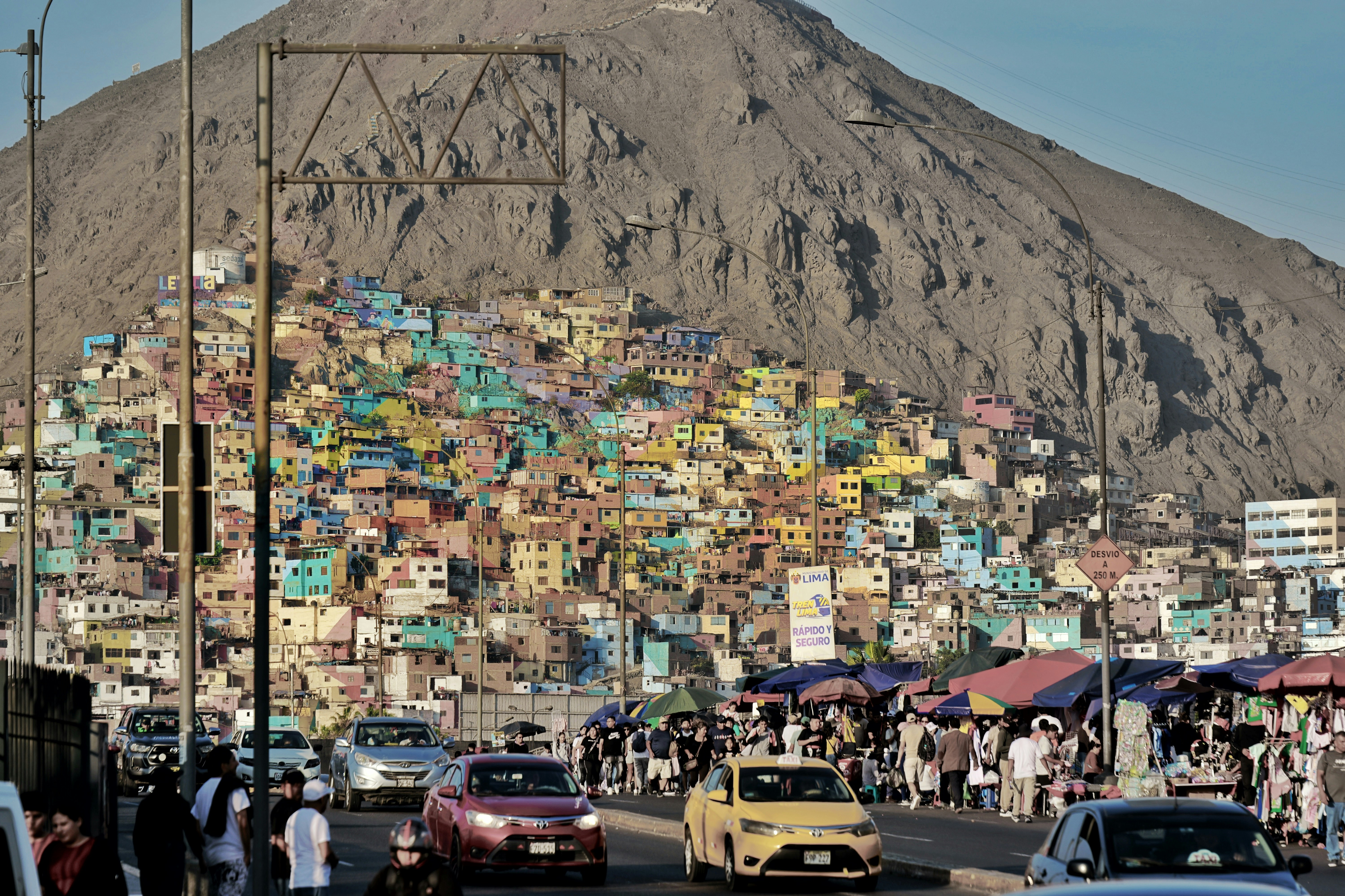 Colorful hillside homes overlook busy street market and traffic.