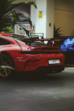 Red porsche 911 parked indoors with plants in foreground.