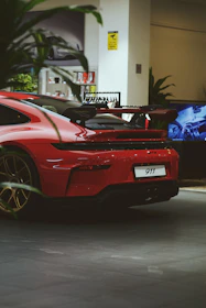 Red porsche 911 parked indoors with plants in foreground.