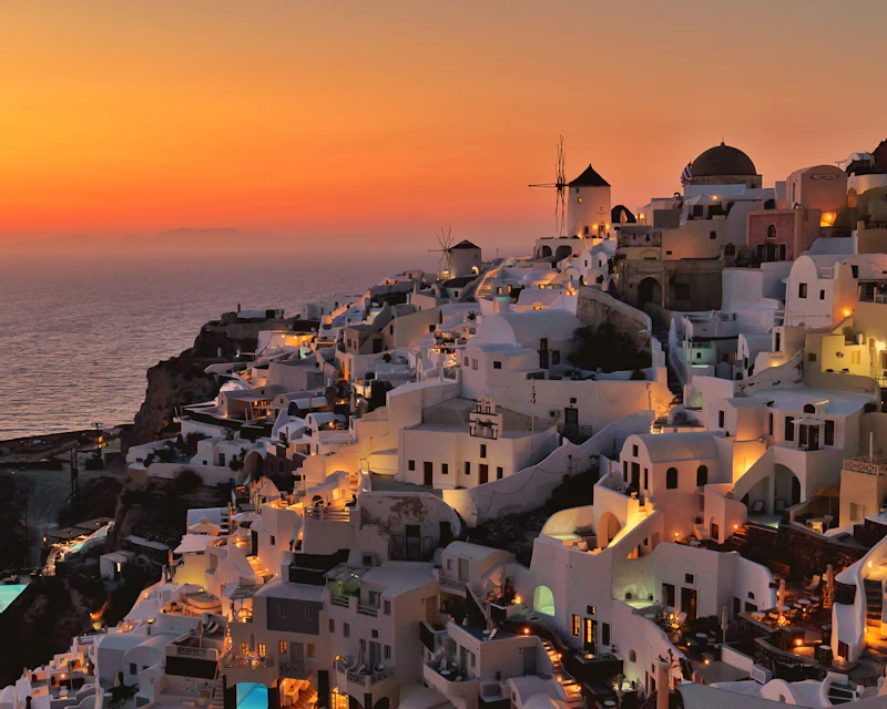 Whitewashed houses and a windmill in Oia, Santorini, glowing at sunset above the Aegean Sea