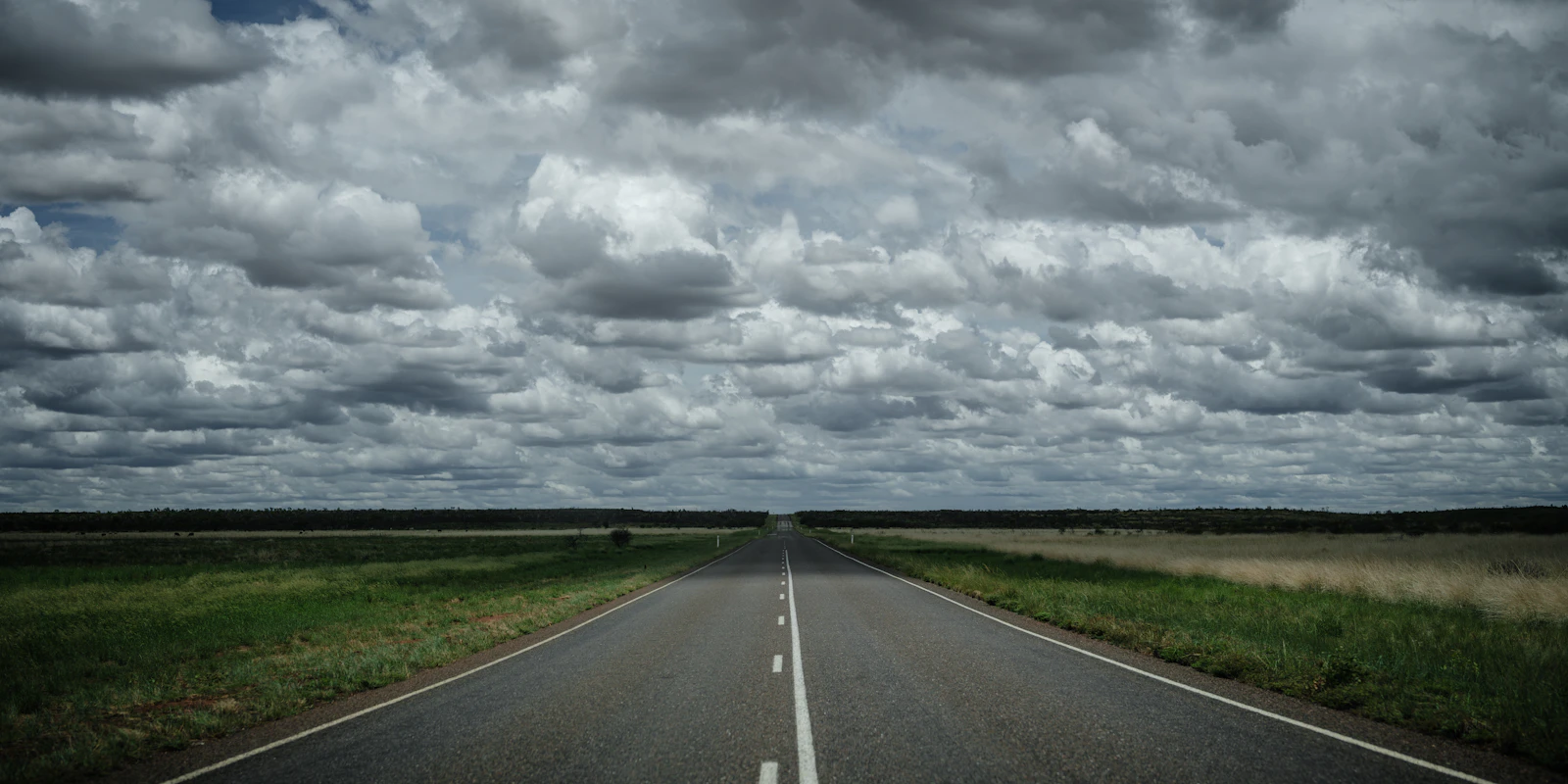 A straight road continues beneath a changing sky in remote Australia