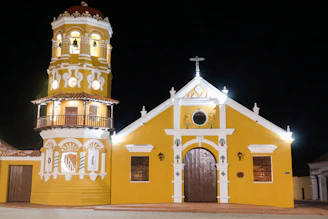 A yellow church with a tall bell tower at night