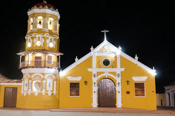 A yellow church with a tall bell tower at night