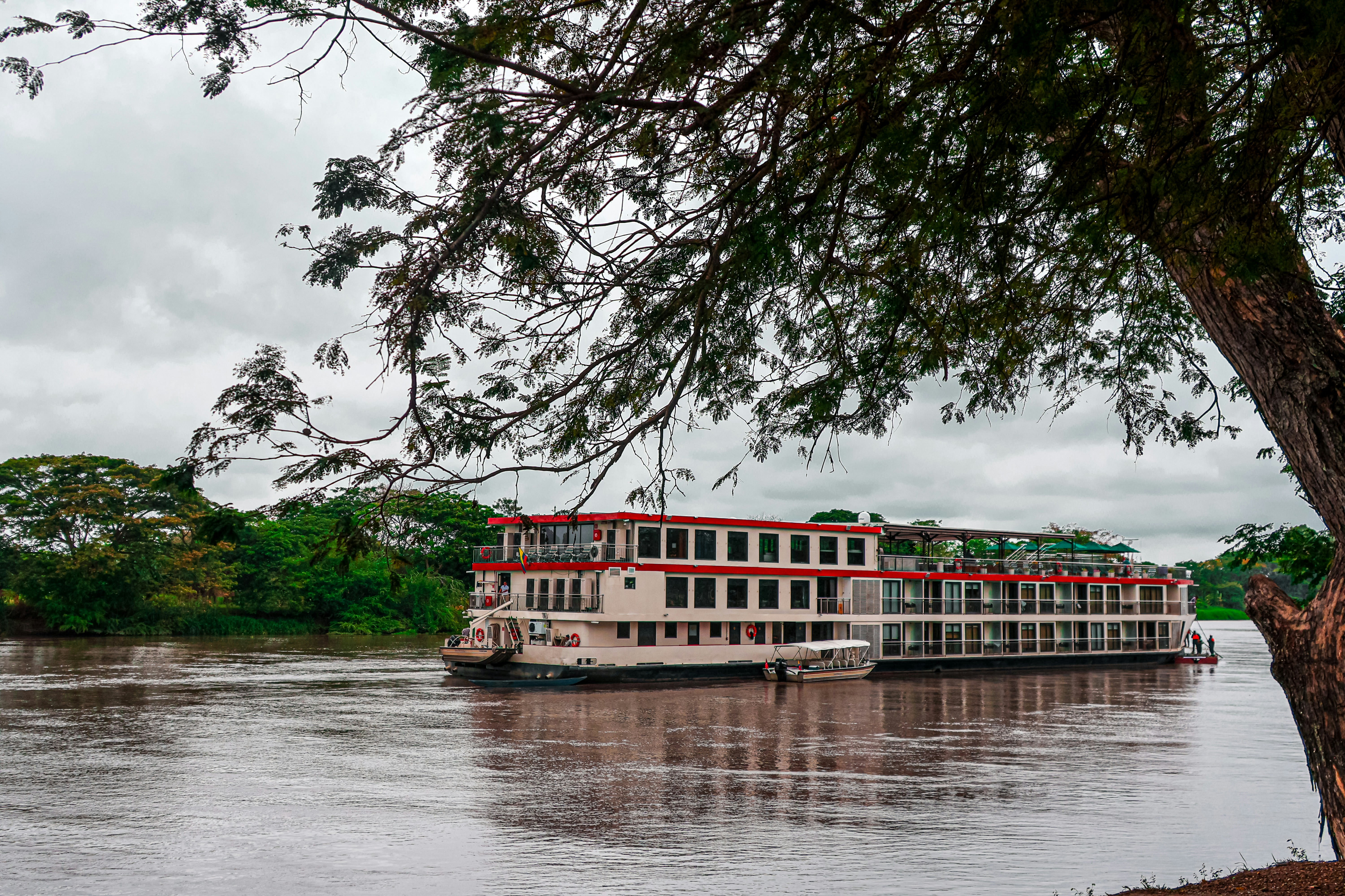 Sebuah perahu sungai besar berlayar menyusuri sungai yang luas dan berlumpur.